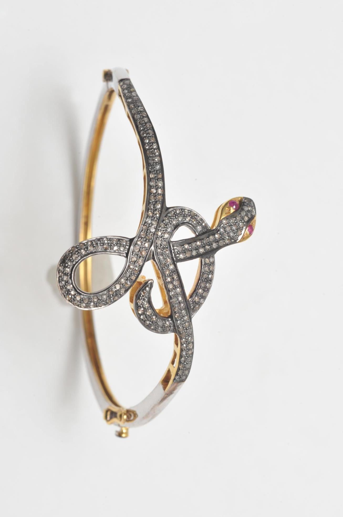 Unusual coiled snake bracelet with pave`-set diamonds and ruby eyes.  18K vermeil along the sides.  Oval shape to keep the diamonds and design on the top of the wrist.  Simple sterling along the back.  Diamond push clasp with two safeties.  Interior
