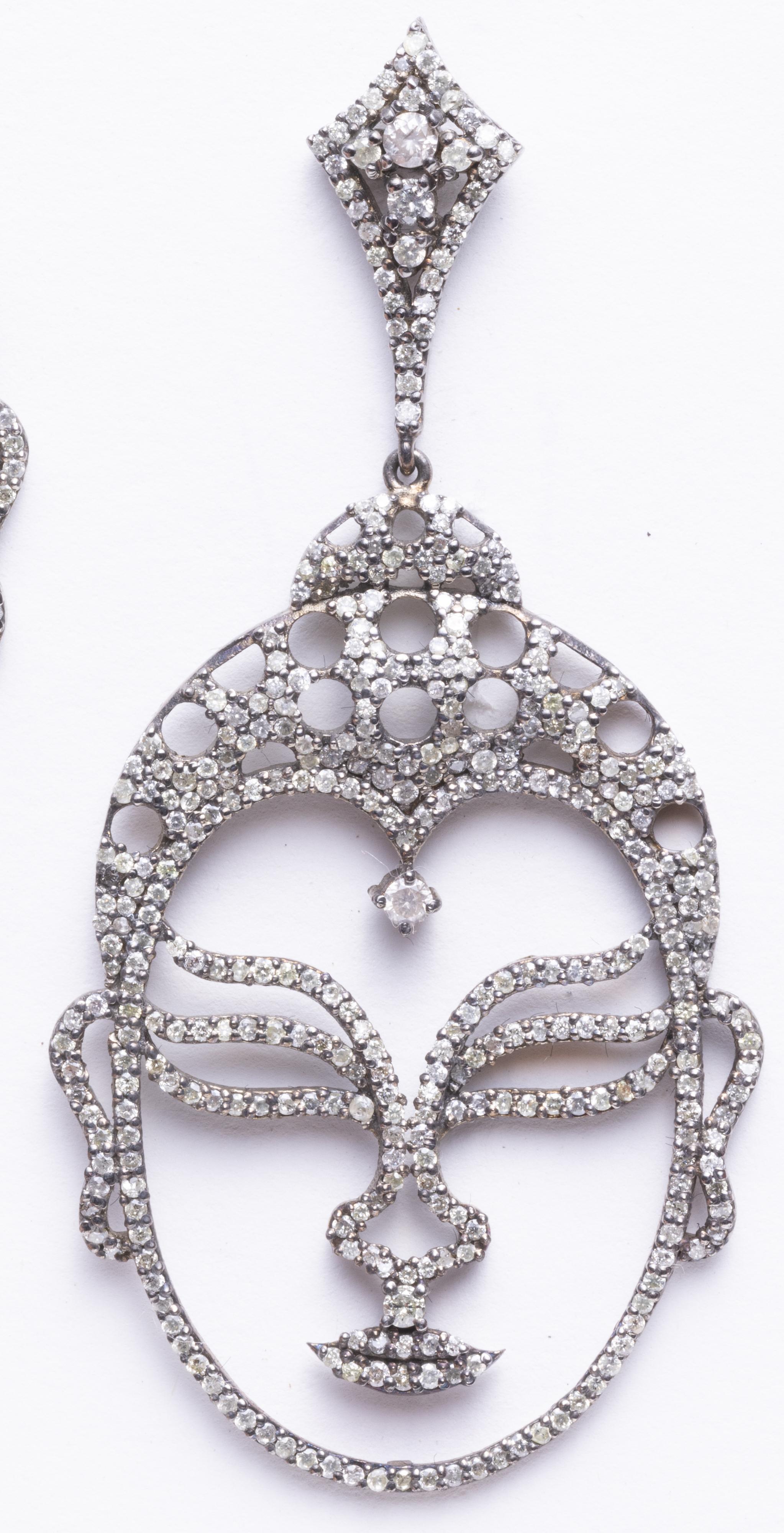 Das Antlitz Buddhas in einem Paar Diamantohrringe.  Runde Diamanten im Brillantschliff in einer Pave-Fassung aus Sterlingsilber und 18-karätigem Gold für durchbohrte Ohren.  Das Gesicht des Buddha enthält ein diamantenes drittes Auge (urna), das die