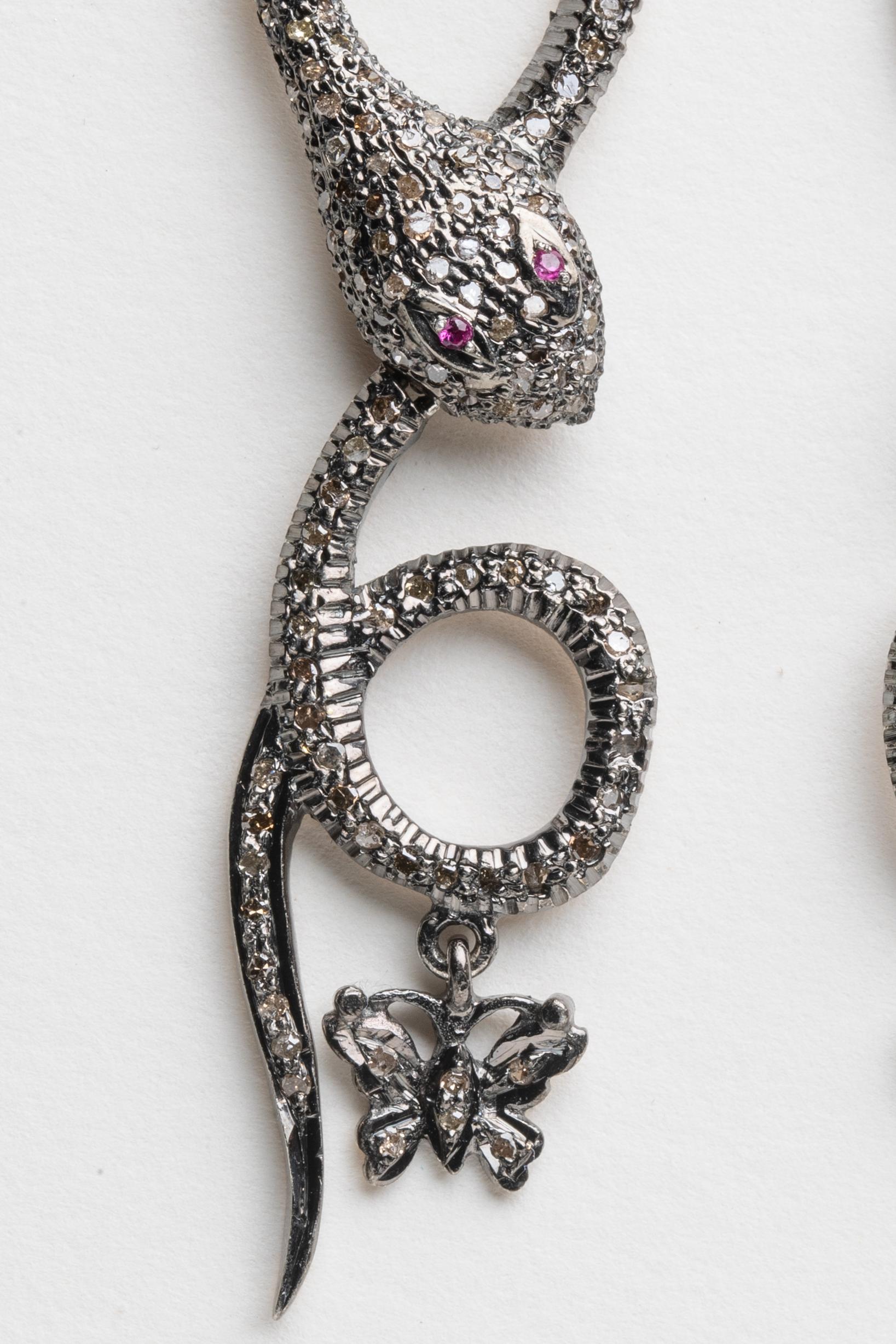 An unusual pair of snake earrings coiled and eyeing the dangling butterfly below.  Pave`-set diamonds and ruby eyes in an oxidized sterling silver with 18K gold post for pierced ears.  Carat weight of diamonds is 2.72.
