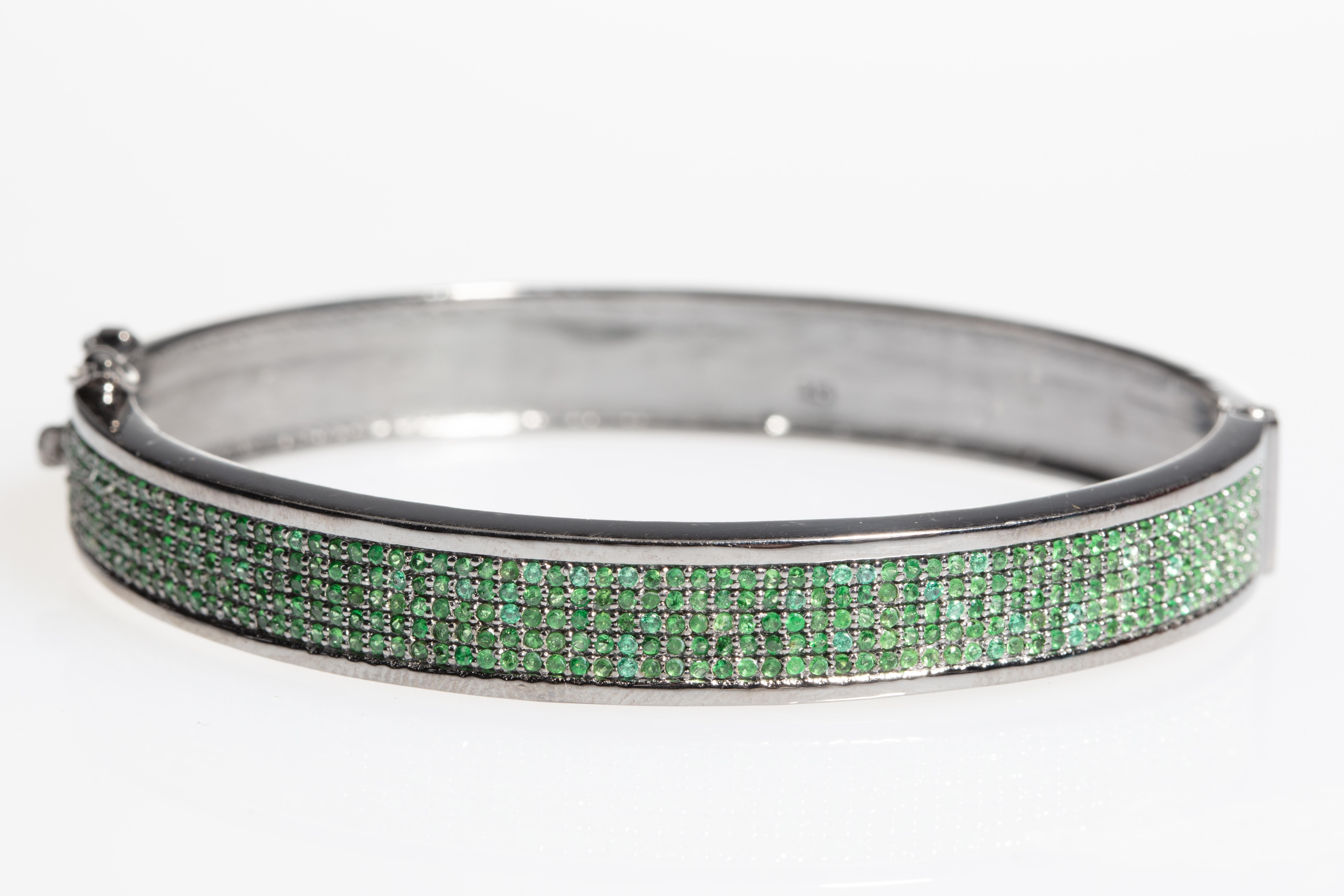 An oxidized sterling silver, oval-shaped bangle with 5 lines of brilliant-cut emeralds in a pave' setting.  Push clasp with side safety.  Weight of emeralds is 1.77 carats.  Oval shape keeps the emerald embellishment on top of the wrist, yet easily