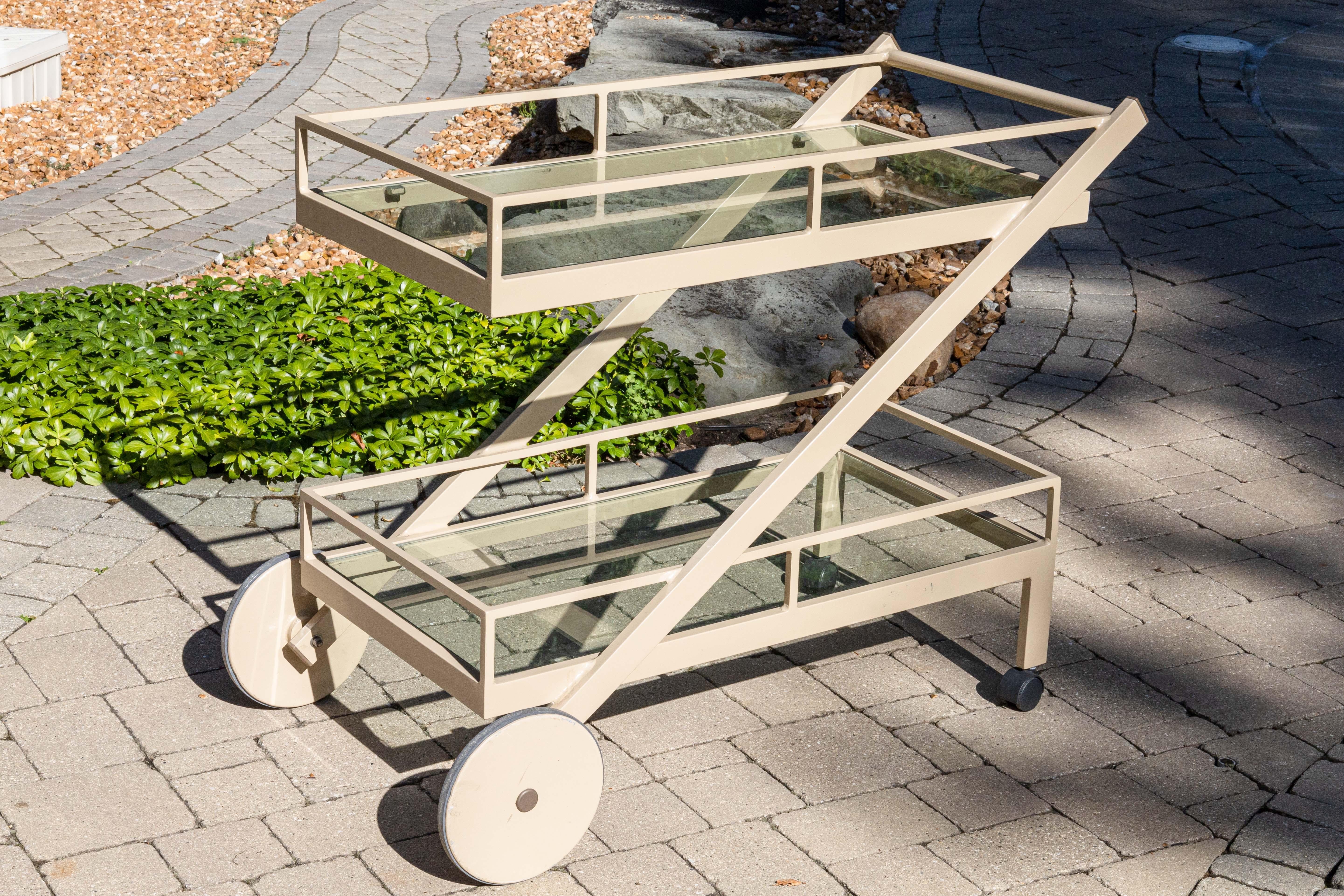 Un carro bar del servicio Pavilion Aventura. Esta encantadora pieza de patio presenta un maravilloso diseño moderno. Está fabricada con aluminio rectangular y tubular, y tiene dos niveles de estantes rectangulares de cristal. La base cuenta con dos