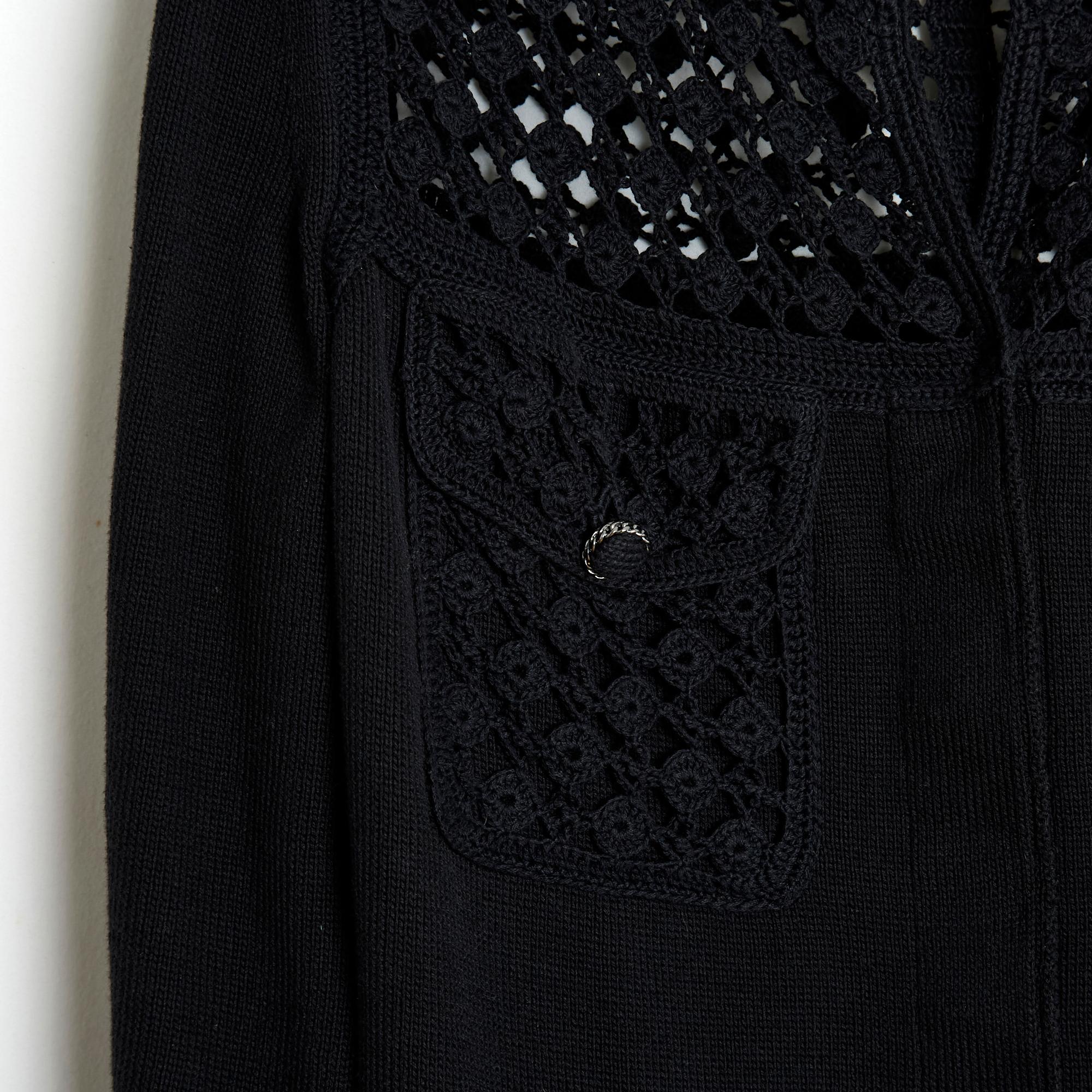 Cardigan Chanel de la collection Printemps Eté 2006, comme une petite veste noire en maille de coton et crochet, col rond fermé par 4 boutons Chanel cachés, manches 2/3, 4 poches à rabat fermées par un bouton, buste supérieur ajouré, non doublé .