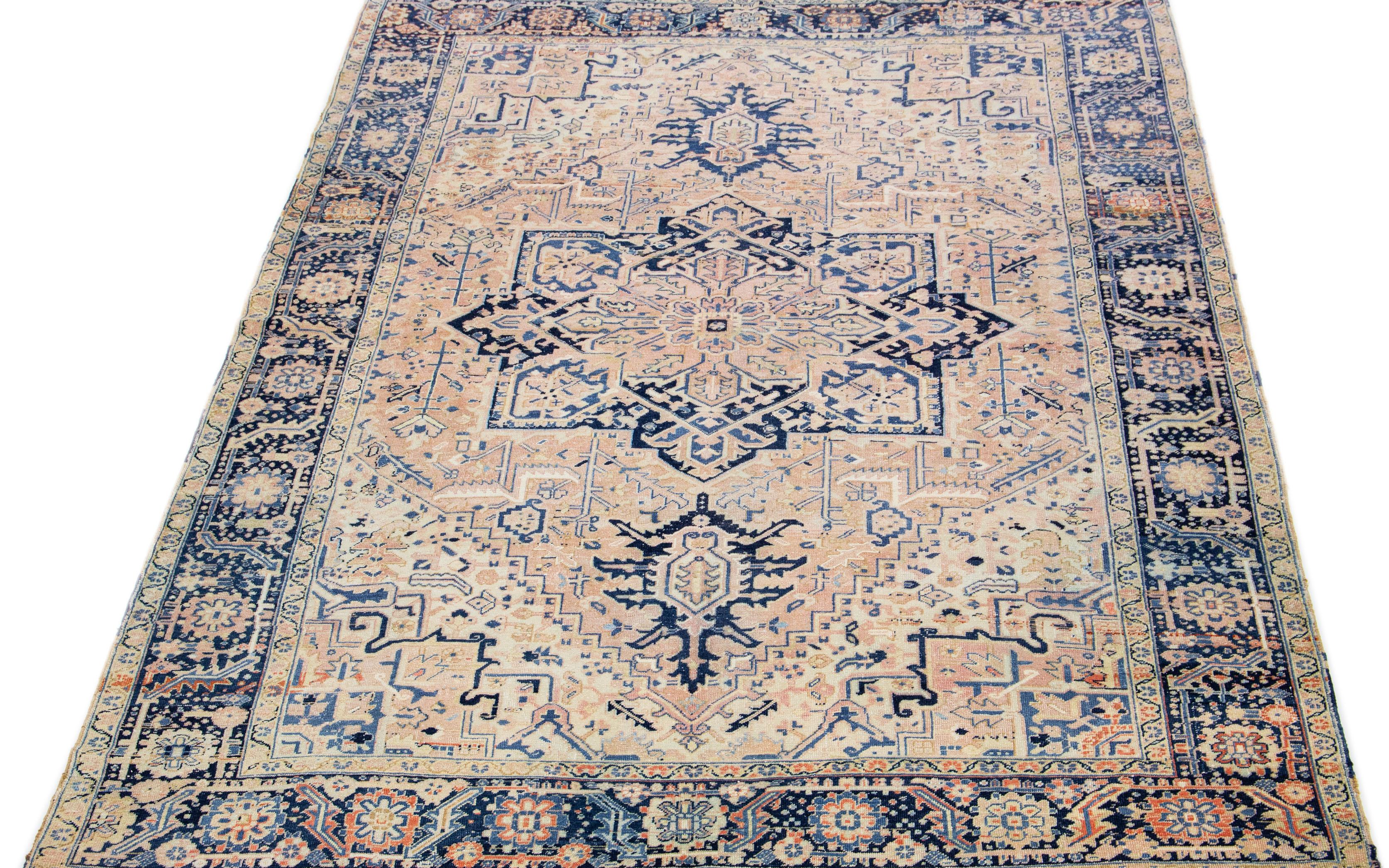 This Persian rug showcases a stunning all-over layout geometric medallion floral motif in shades of blue and ivory, set against a peach and beige field. Crafted from luxurious hand-knotted wool, this antique Heriz rug exudes timeless