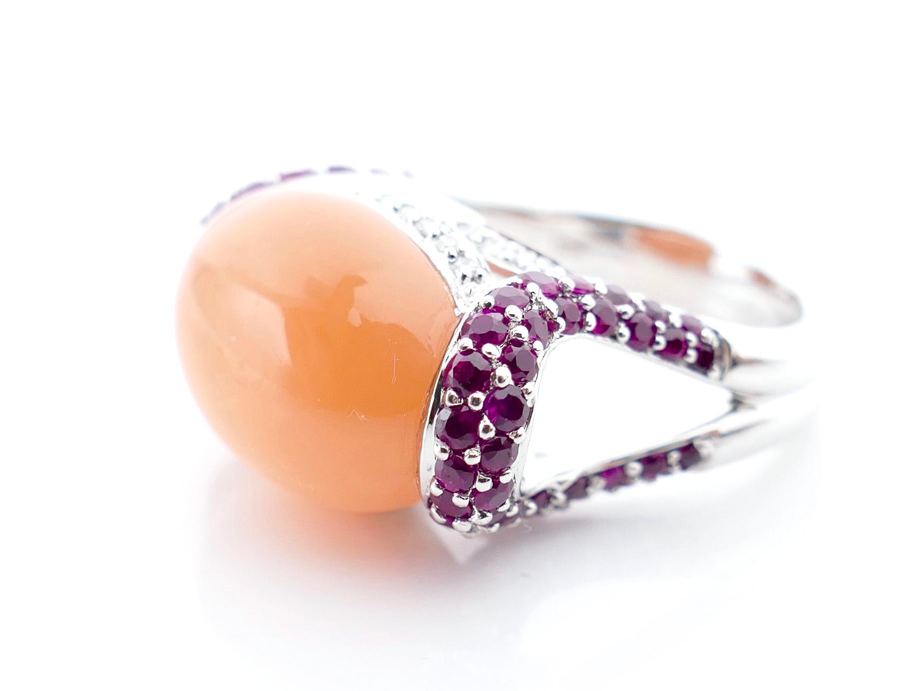 This stylish peach Carnelian cabochon ring makes an unforgettable fashion statement. With 70 pave-set Rubies and 32 pave-set Diamonds, weighing in at 2 Carats total, the ring shines with color. The base is made of 14K White Gold and has an open,