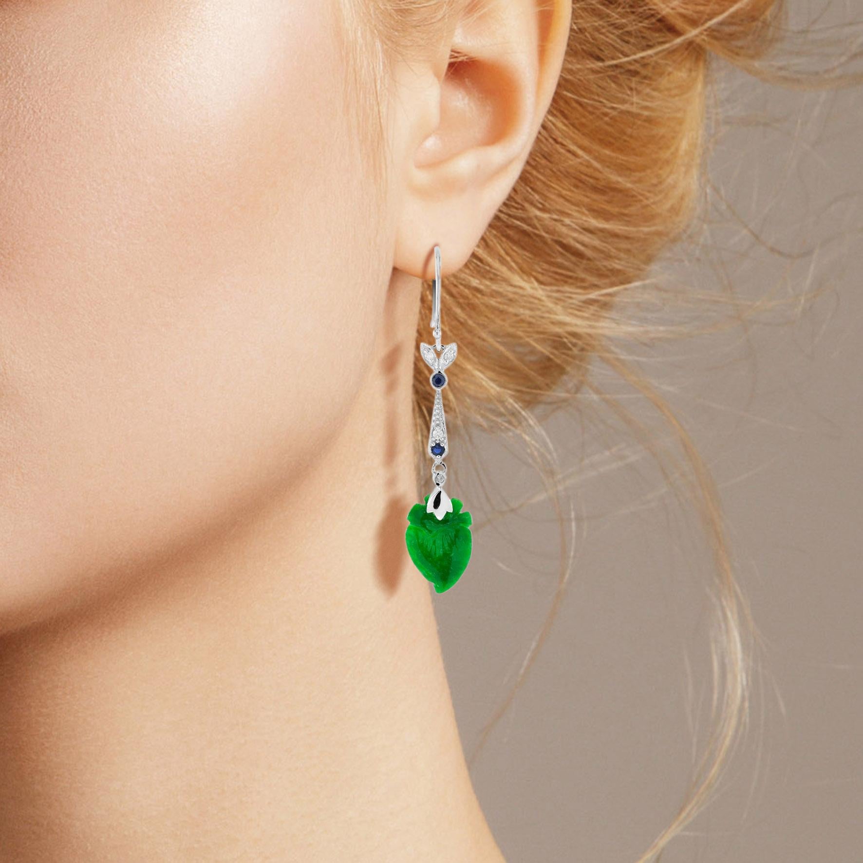 The natural jade in these lovely earrings has some very special shape. Both pieces have a strong green color and well peach fruit carvings. The jade is suspended in a 9k white gold setting with diamond leaf and round blue sapphires on the top. The