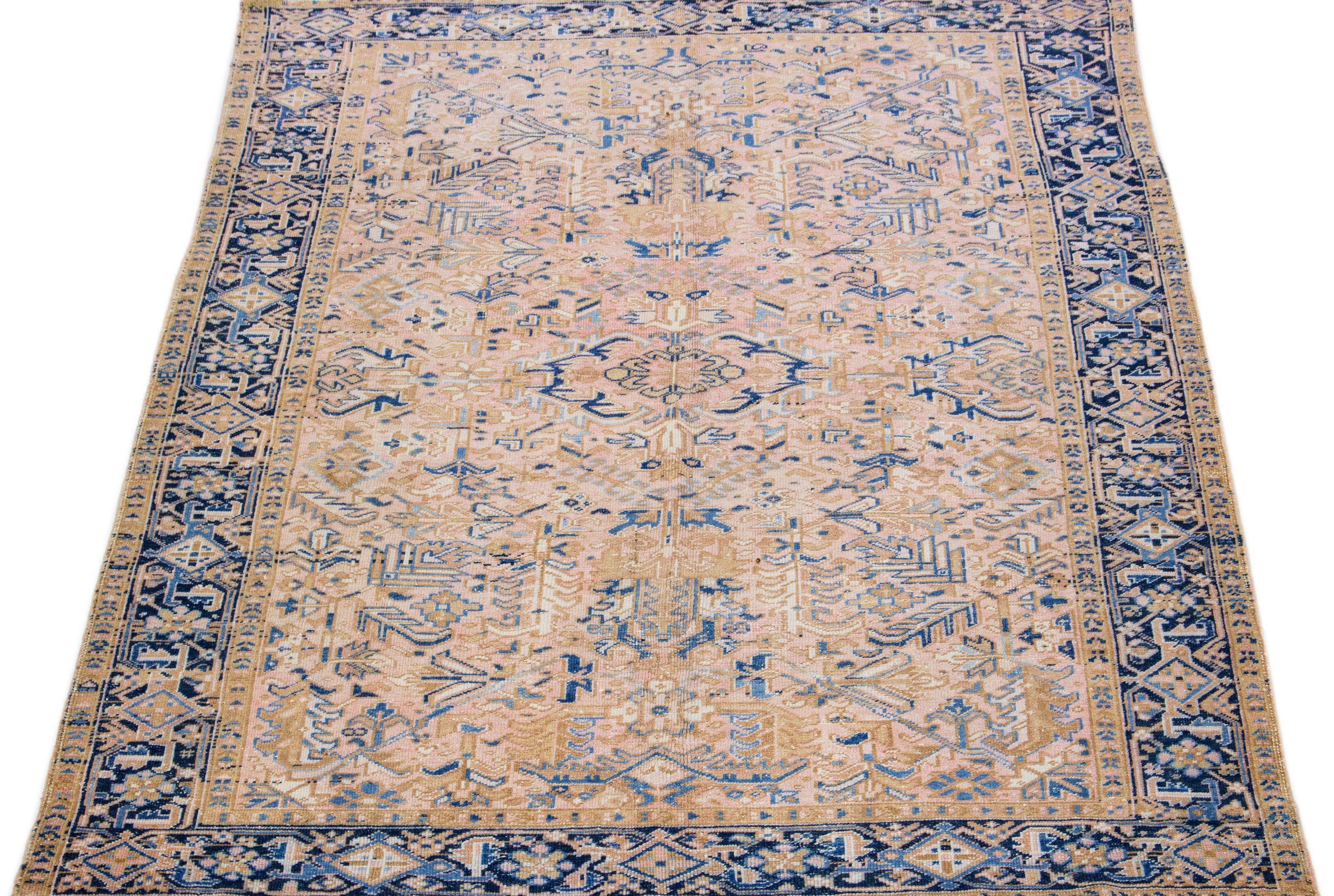 This Persian rug boasts a splendid all-over design with an eye-catching geometric floral pattern in shades of blue and brown set against a soft peach field. Using premium hand-knotted wool, this antique Heriz rug radiates eternal class and