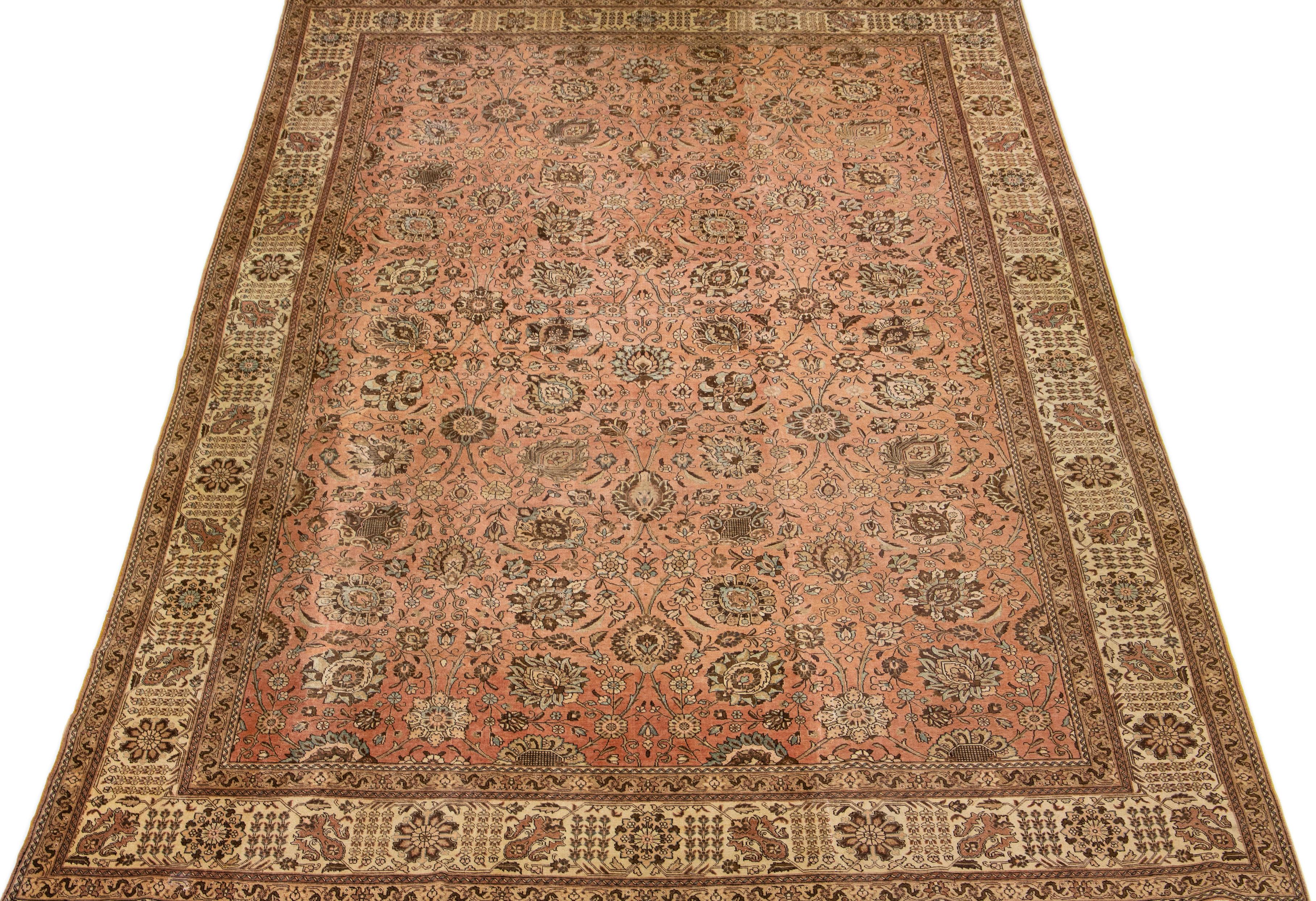 This Persian Tabriz wool rug showcases an exquisite traditional floral medallion design with striking beige, blue, and brown accents against a peach background. 

This rug measures 11'10