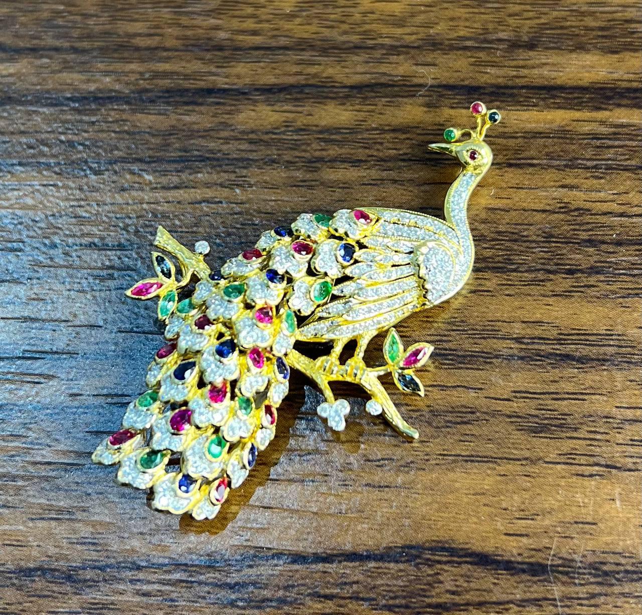 This exquisite piece is crafted in 14k solid gold and features a detailed peacock design perched on a branch.

The body and tail are adorned with an array of colorful gemstones, including vibrant red rubies, green emeralds, and blue sapphires, each