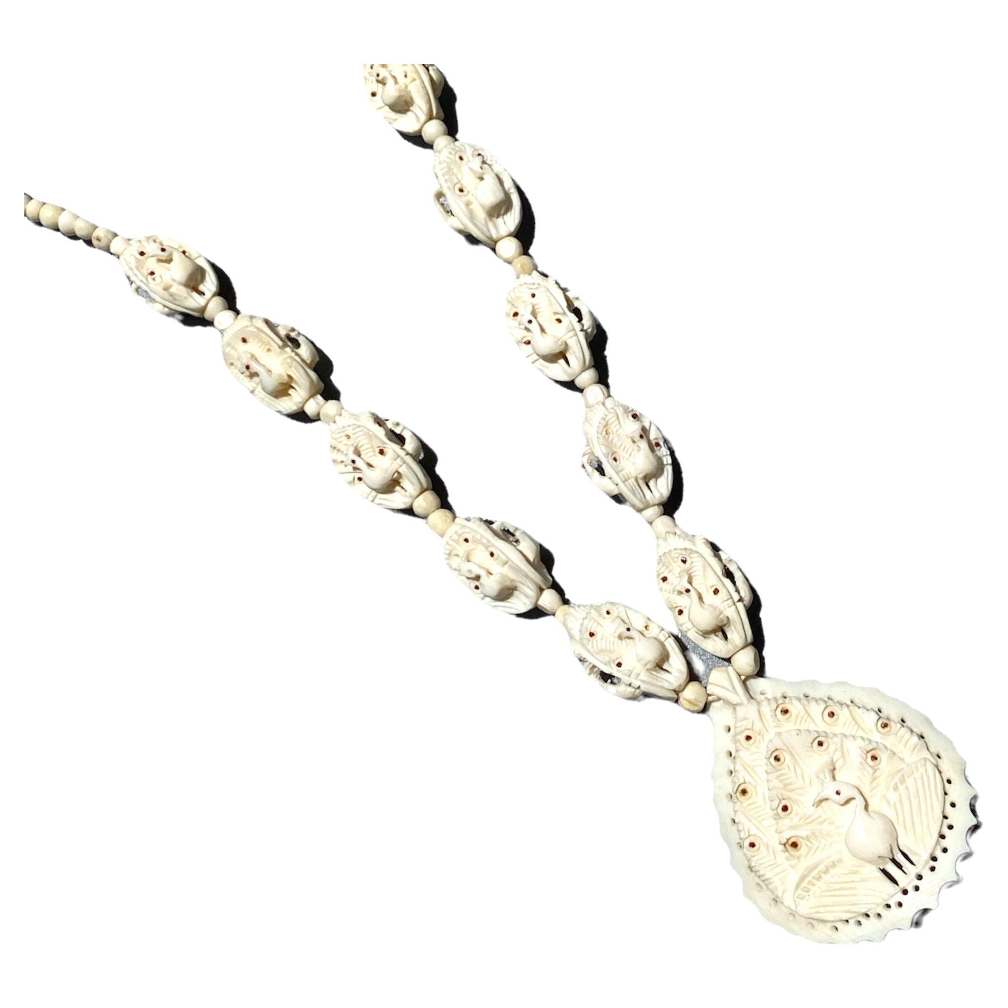  10 perle di pavone intagliate si estendono su una collana di 16 pollici. 
Le perline color avorio misurano 12 mm x 18 1/2 mm e aumentano fino a 21 mm di lunghezza più vicino a un ciondolo pendente.

Il ciondolo a forma di pavone misura 42 1/2 x 40