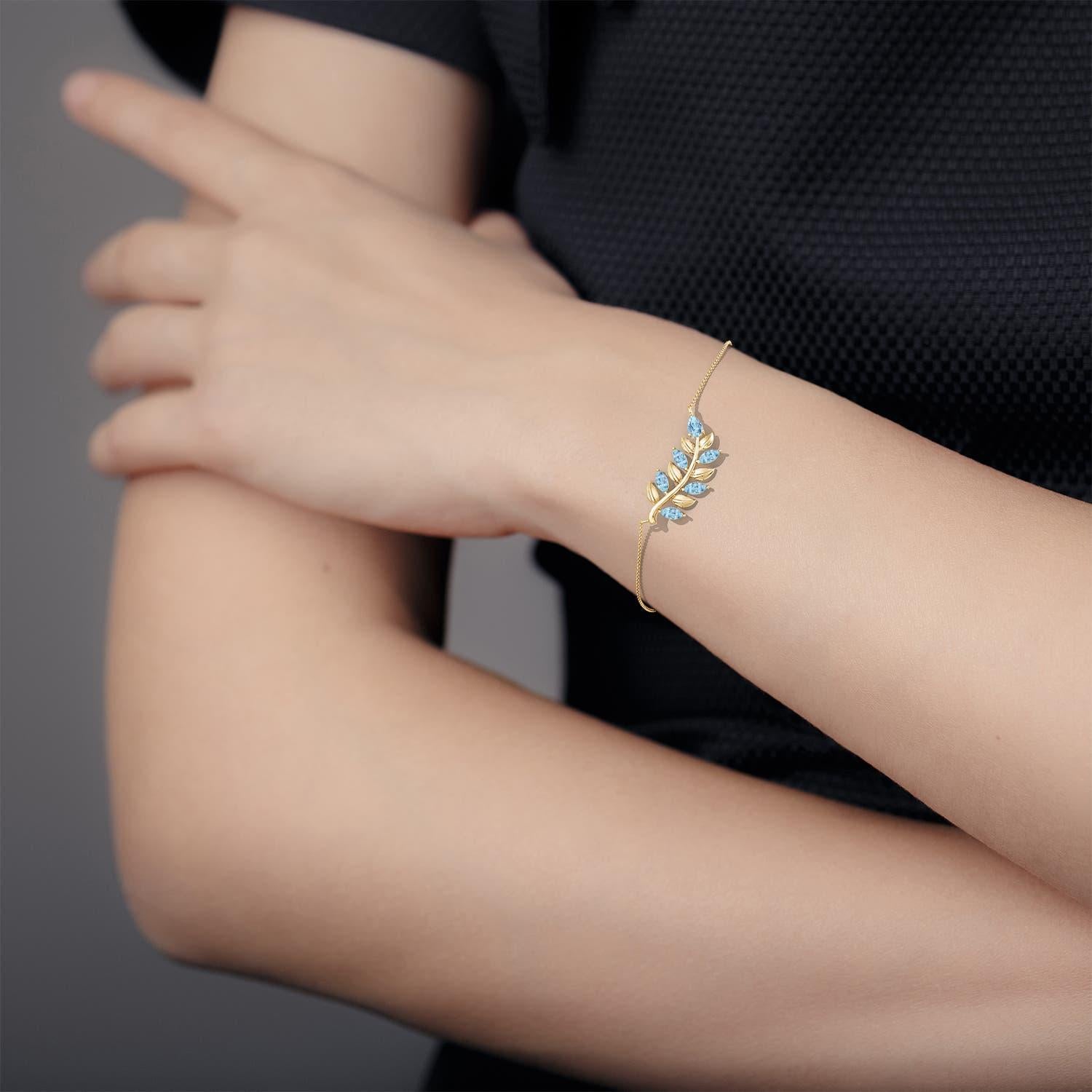 This olive branch bracelet is a stunning symbol of peace and victory. It showcases pear-shaped and marquise aquamarines that exude an icy blue hue. The leaf motifs enhance the overall allure of this 14k yellow gold bracelet.