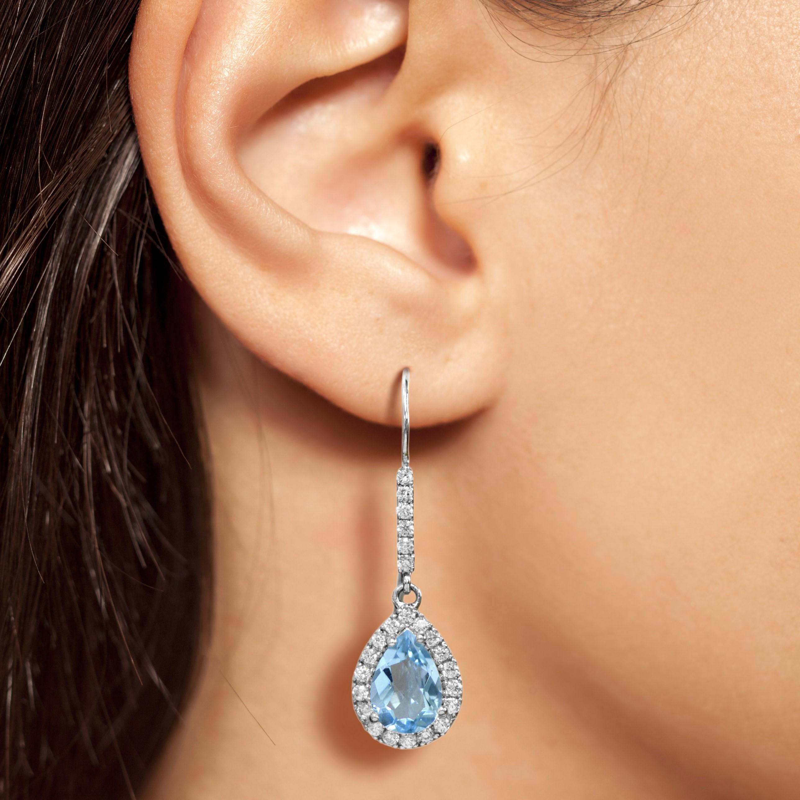 Ces boucles d'oreilles halo en topaze bleue sont d'une beauté luxueuse en or blanc 14K. Un halo de diamants souligne la teinte bleue estivale de la pierre précieuse. Des diamants étincelants ornent la balle d'une brillance supplémentaire. Un cadeau