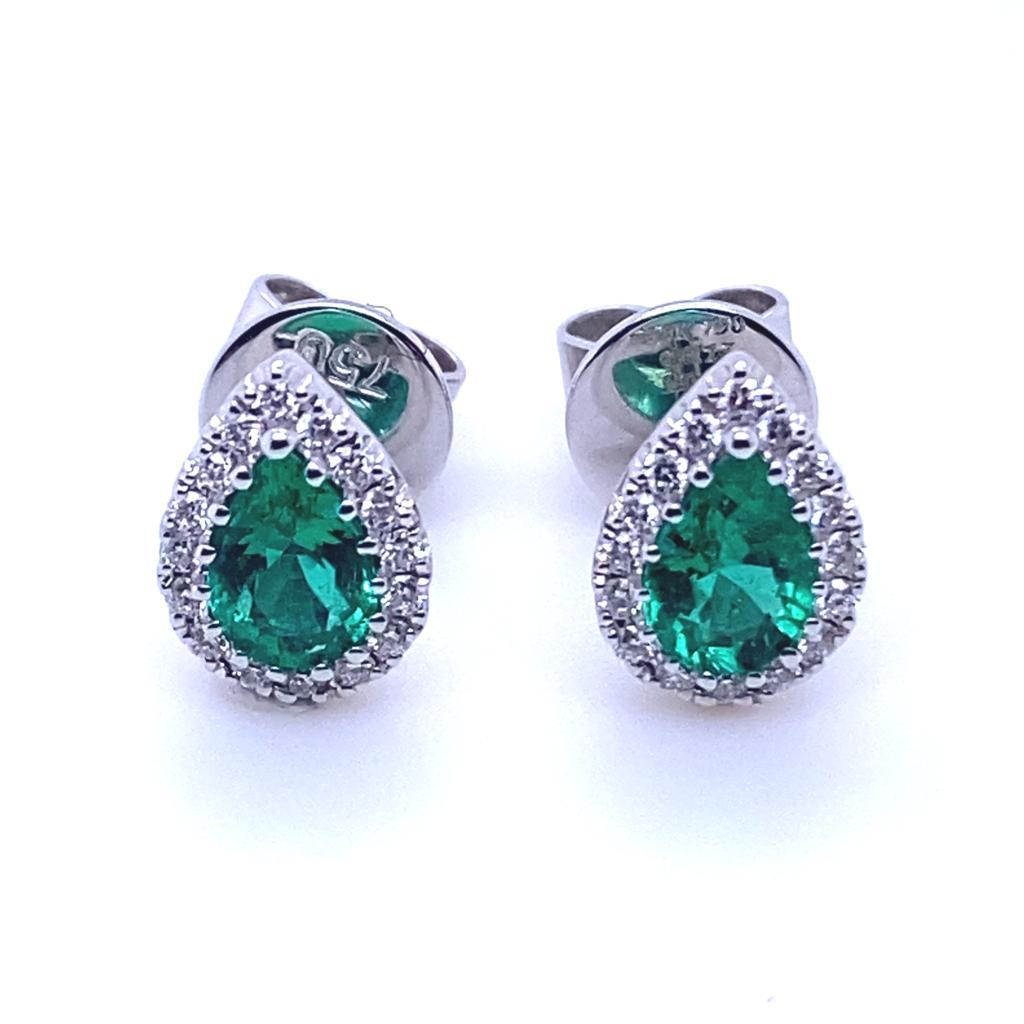 A pair of pear cut emerald and diamond cluster earrings in 18 karat white gold.

Each of these stud earrings comprise of a beautiful pear cut deep green emerald of fine quality surrounded by a claw set halo of sparkling round brilliant cut diamonds.