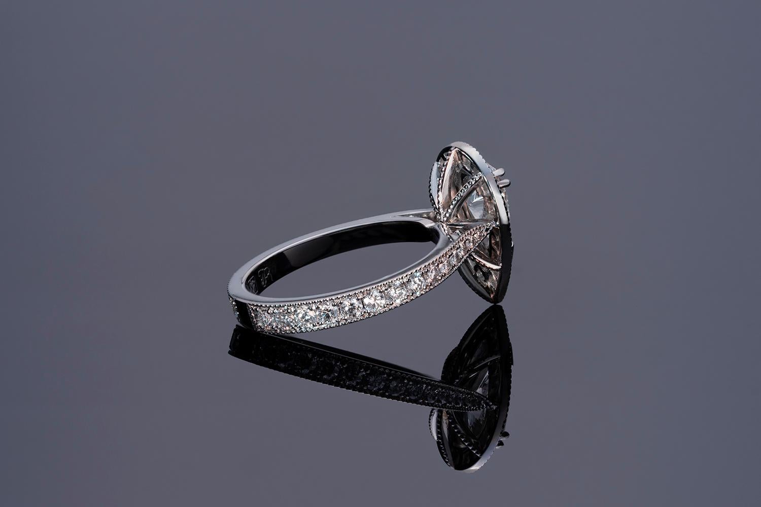 The ring features a single Pear Cut diamond, claw set on a floating mount, surrounded by a millgrained and threadset border of Round Brilliant Cut diamonds.

The gallery features hand-millgrained wire work, and is set on a tapered band, millgrained