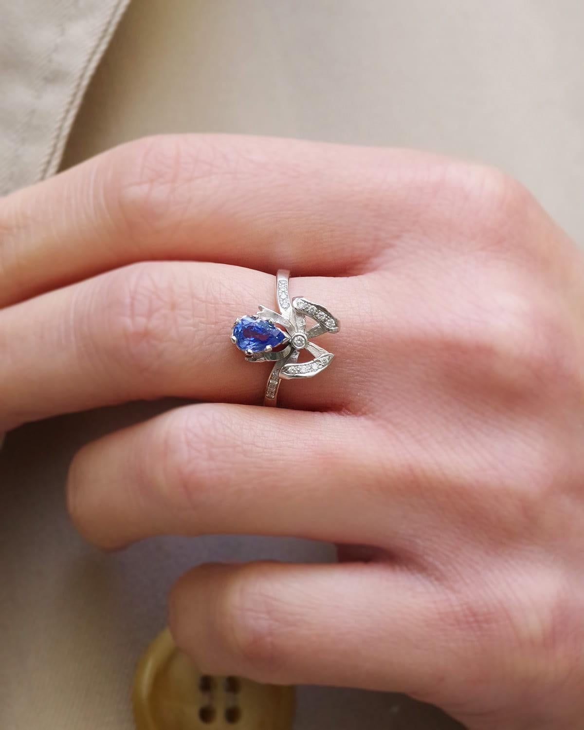 Pear-cut sapphire bow ring in 18 karat white gold. A Belle Epoque-style knot ring, set with a 0.76-carat pear-shaped sapphire and 0.11 carats of brilliant-cut diamonds. The sapphire has a beautiful, intense sky blue color. A Belle Epoque-style ring,