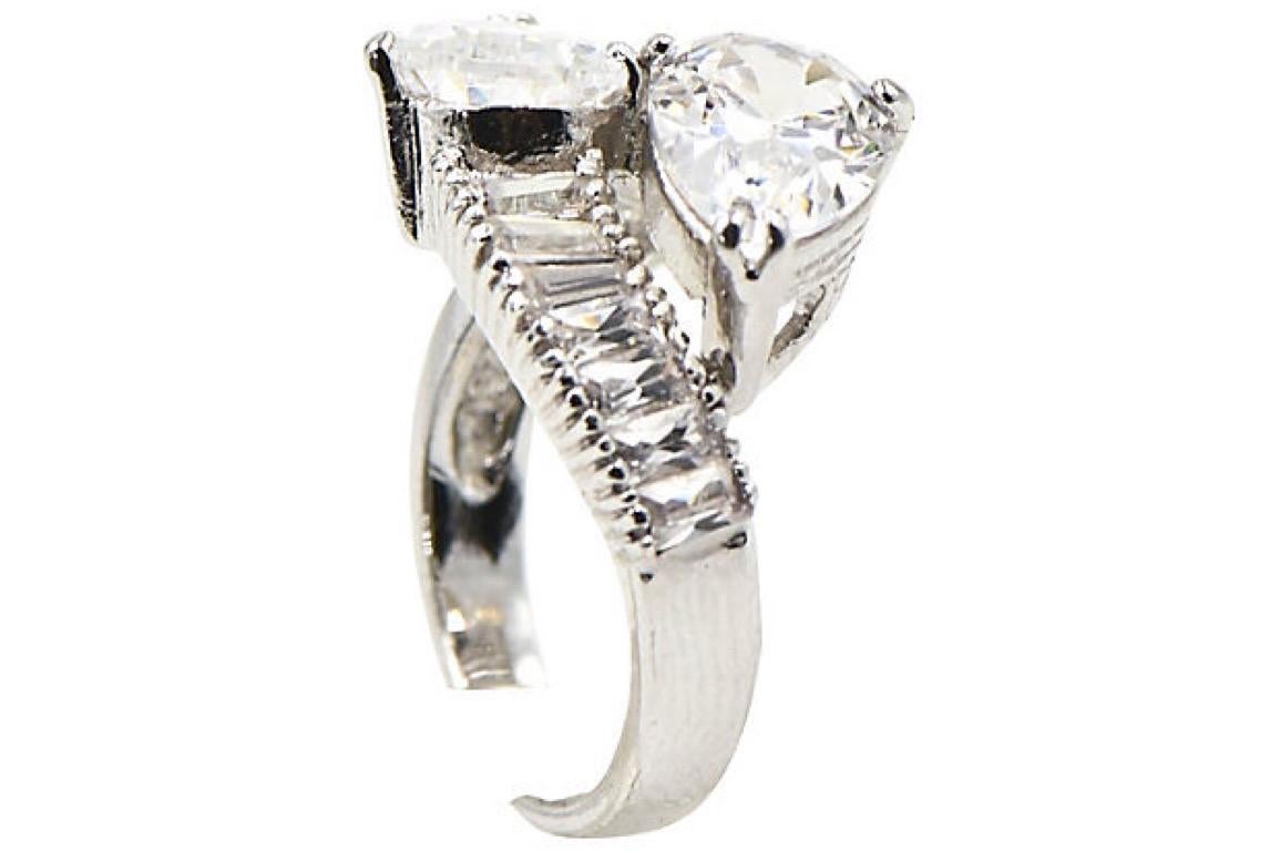 Impressive costume cubic zirconia (CZ) cocktail ring that imitates a pear shaped diamond bypass ring. The pear CZs look like 2.75 carat each diamonds mounted with baguettes in rodium plated sterling silver hardware. Marked 925 for sterling silver.

