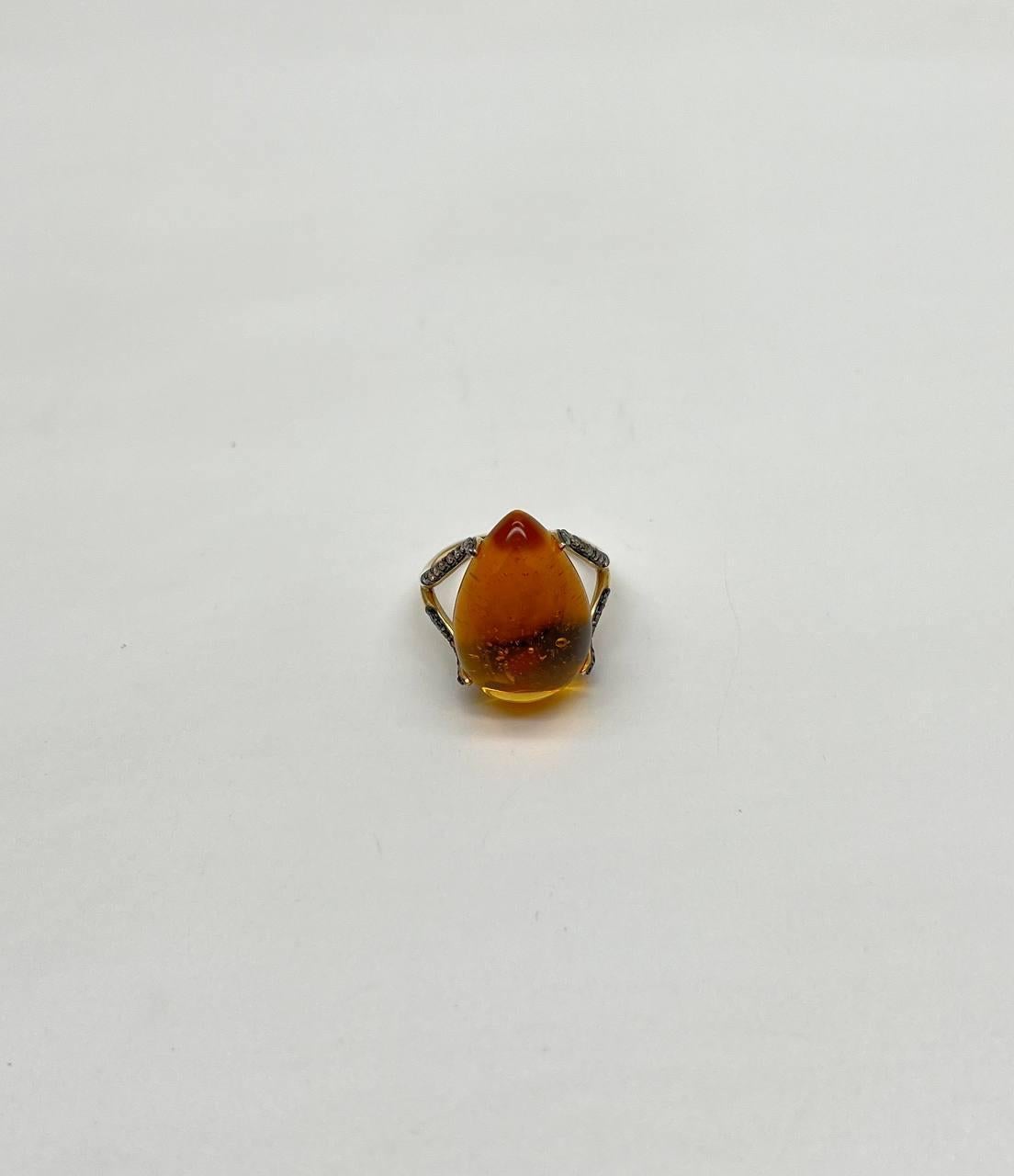Questo squisito anello è caratterizzato da un sorprendente citrino arancione color ambra con una forma a goccia cabochon. La pietra è incastonata in una fascia d'oro 14 carati che presenta dettagli intricati sui lati. Le tonalità calde della pietra
