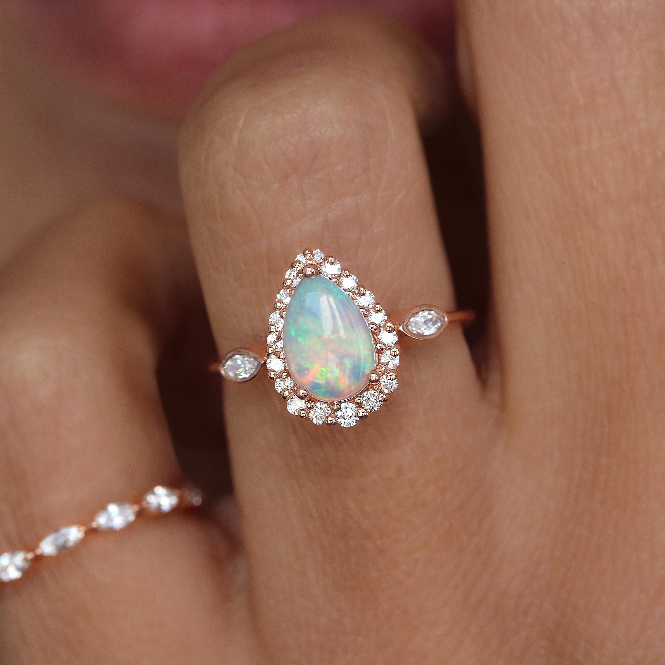 This pear opal halo engagement ring is a stunning piece of jewelry. It features a pear-shaped opal with marquise-cut side diamonds. The combination of hues and shapes creates a unique and eye-catching aesthetic, perfect for saying 