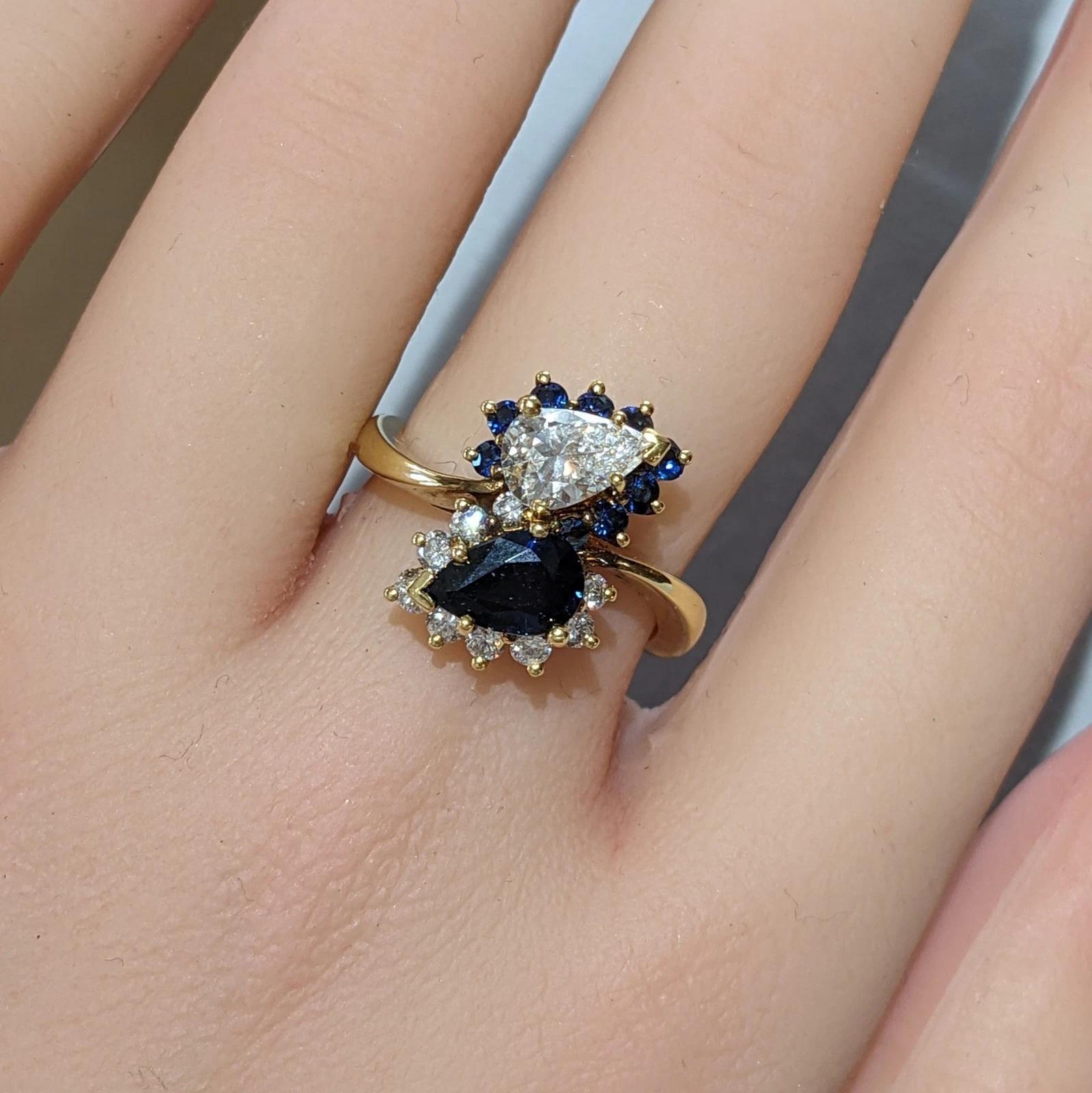 Anello bypass con zaffiro e diamante perlato in oro giallo 18 carati 

L'anello con diamanti e zaffiri naturali presenta un diamante a forma di pera circondato da zaffiri rotondi e uno zaffiro a forma di pera blu scuro circondato da diamanti