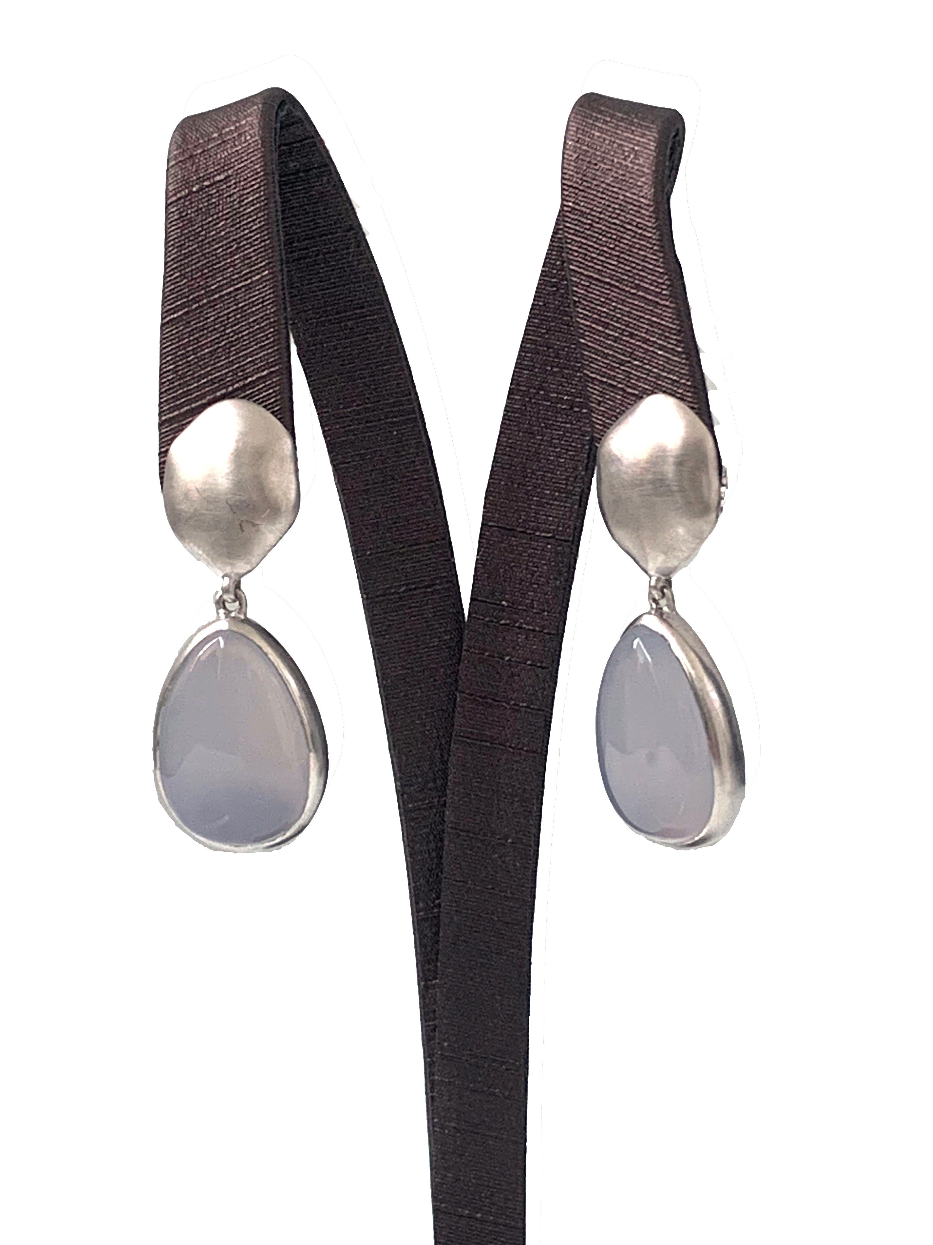 Discover pear-shape Chalcedony drop earrings. The earrings feature 2 large pear-shape cabochon-cut Chalcedony with unique periwinkle purple-ish blue hue, handcrafted brushed satin texturing technique, and hand set in platinum rhodium plated sterling
