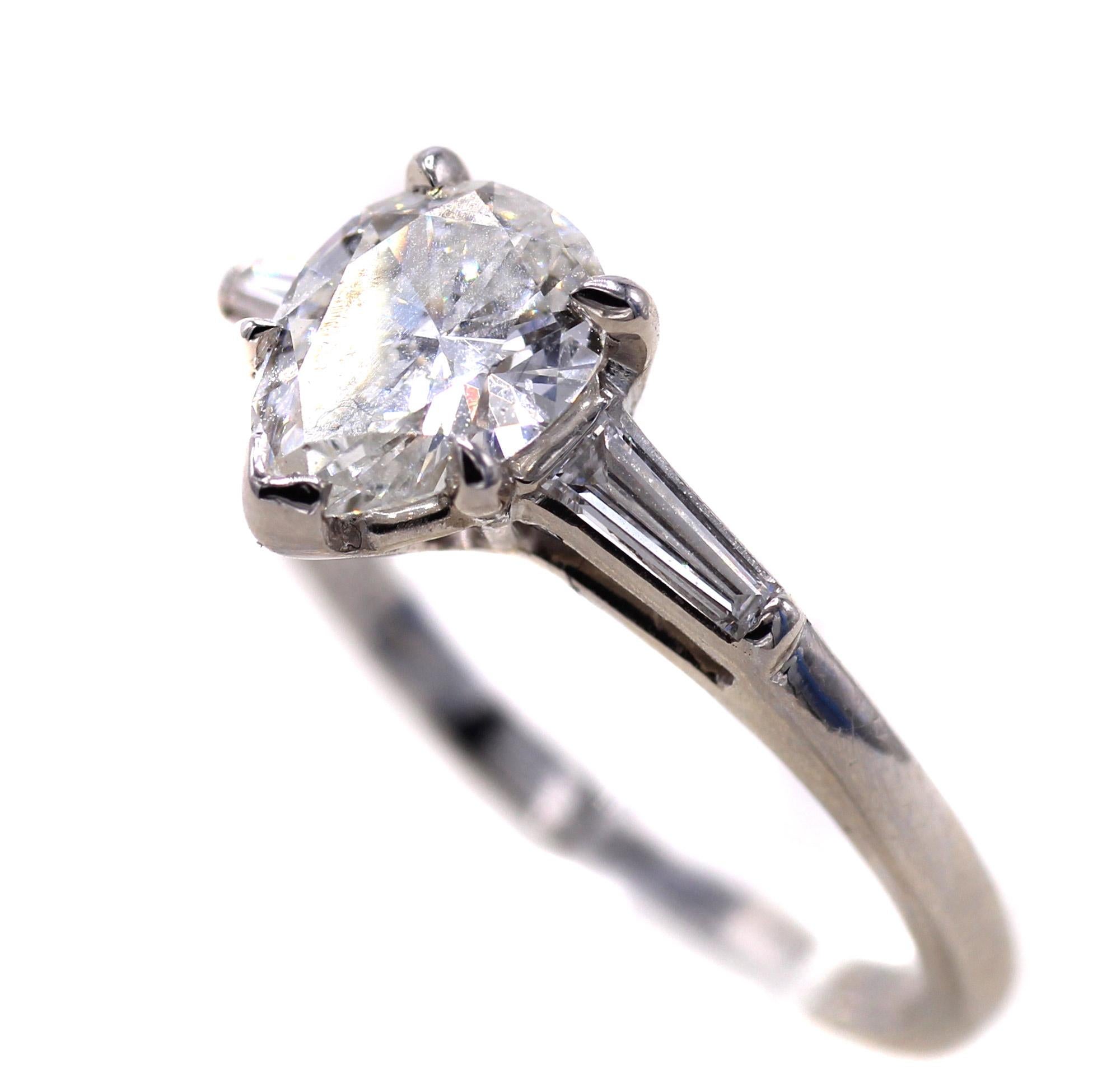 1 carat pear shape diamond is set in a handcrafted platinum mounting set with 2 white bright tapered baguette cut diamonds. The pear shape is accompanied by a report from the GIA giving the diamond a color grade of H and a clarity of I1. The