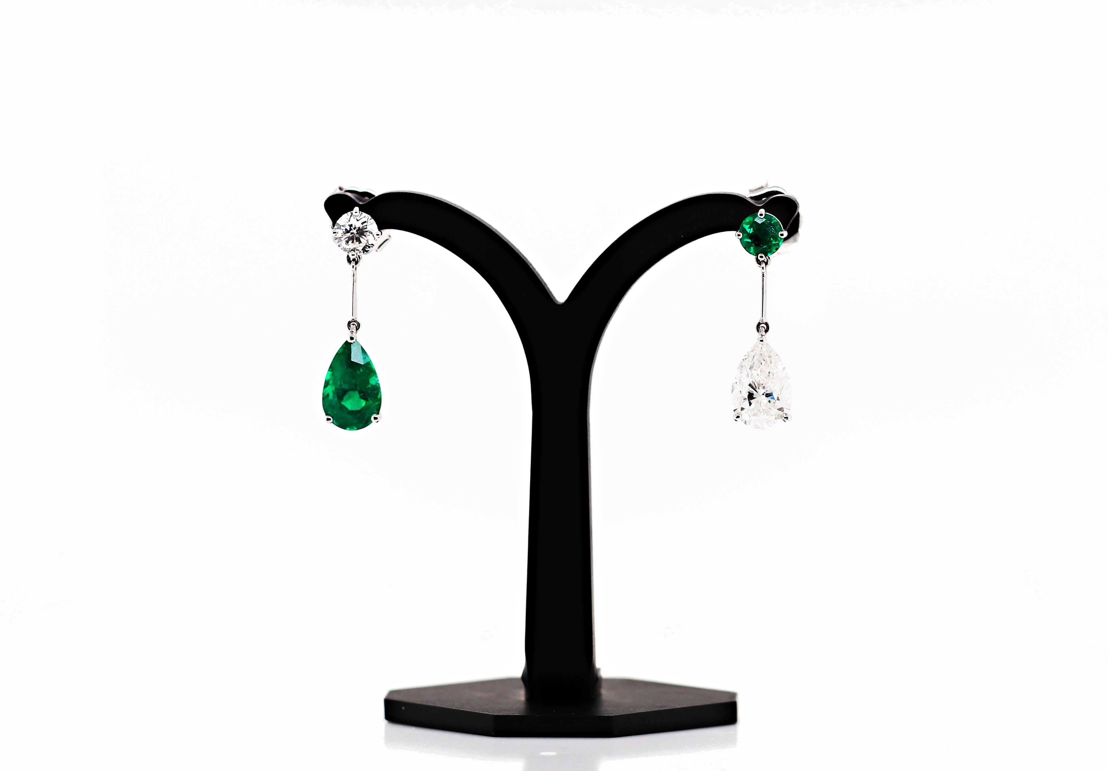 Magnificent unique pair of handmade drop earrings, each featuring an emerald and diamond. The first is set with a vibrant green pear shape emerald weighing 2.97ct in a three claw open back setting, hanging off a round brilliant cut diamond in a four