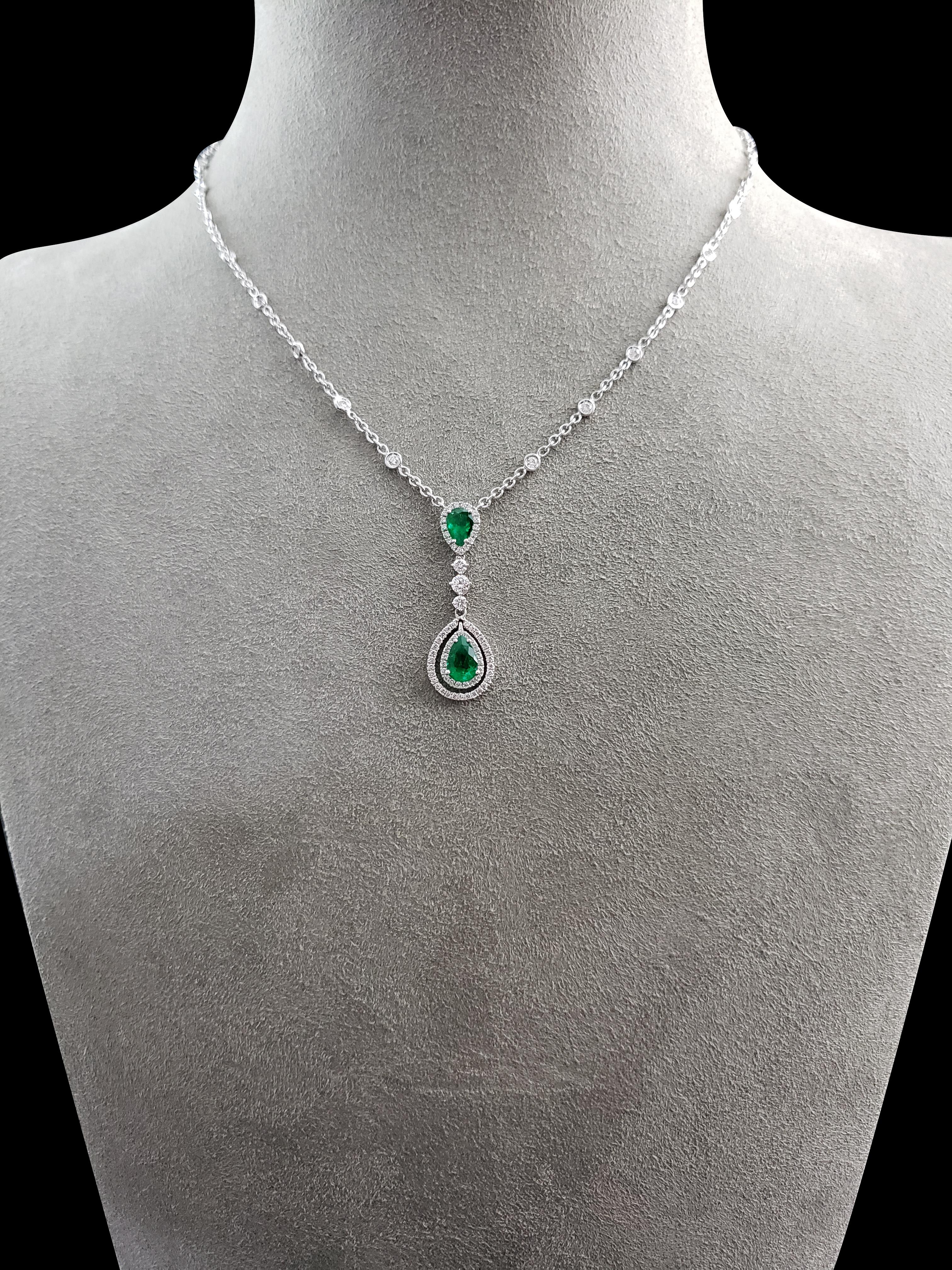 A vibrant pear shape emerald surrounded by 2 rows of sparkling round diamonds, elegantly suspends from another pear shape emerald in a diamond encrusted halo. Each emerald is spaced by a single solitaire diamond. The green emeralds weigh 1.09 carats