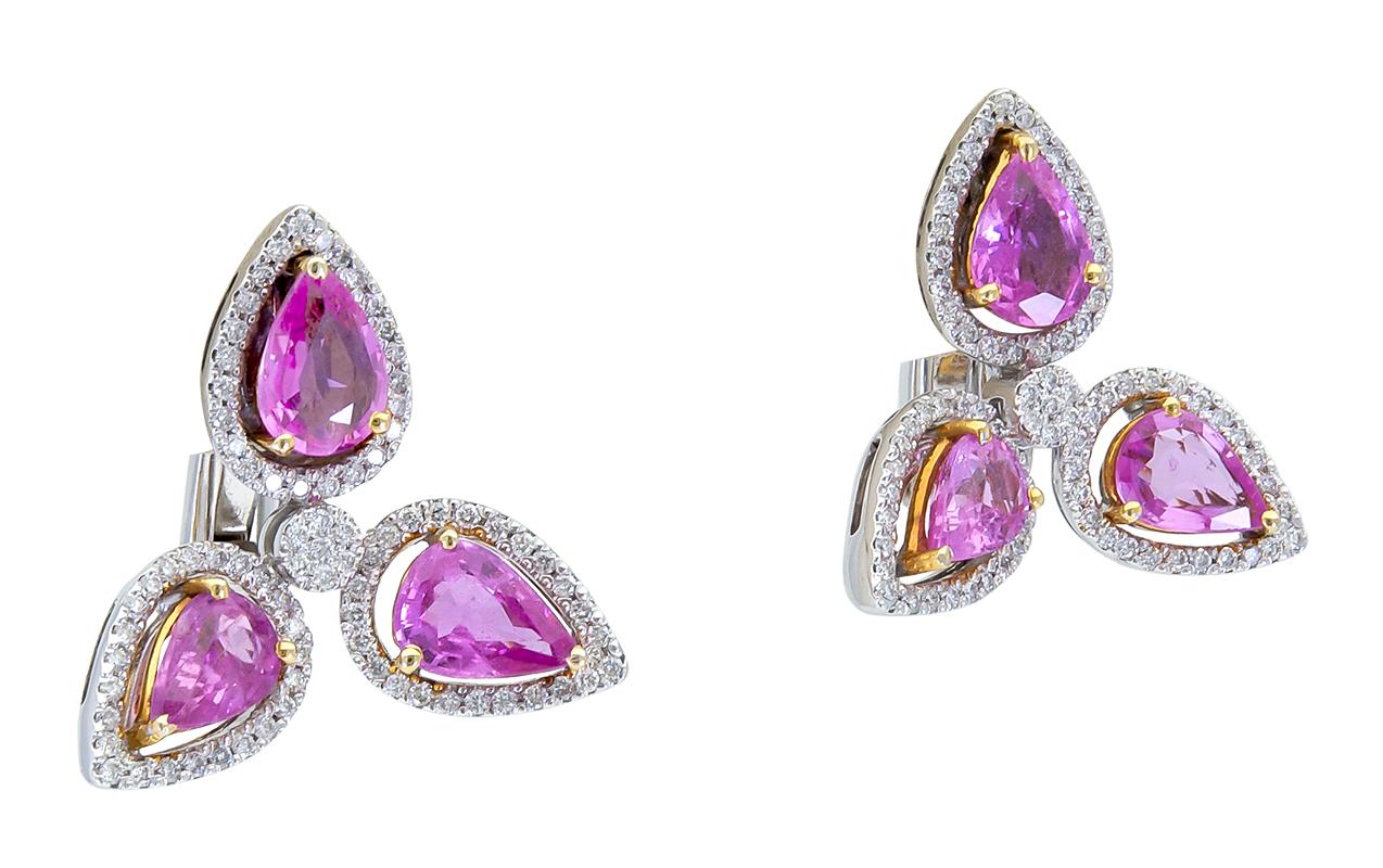 A unique and chic pair of drop earrings. Each earring features three color-rich pink sapphires set in an open-work brilliant diamond halo; attached in a three-point star design. Made in 18k white gold. A magnificent piece of jewelry to add to any