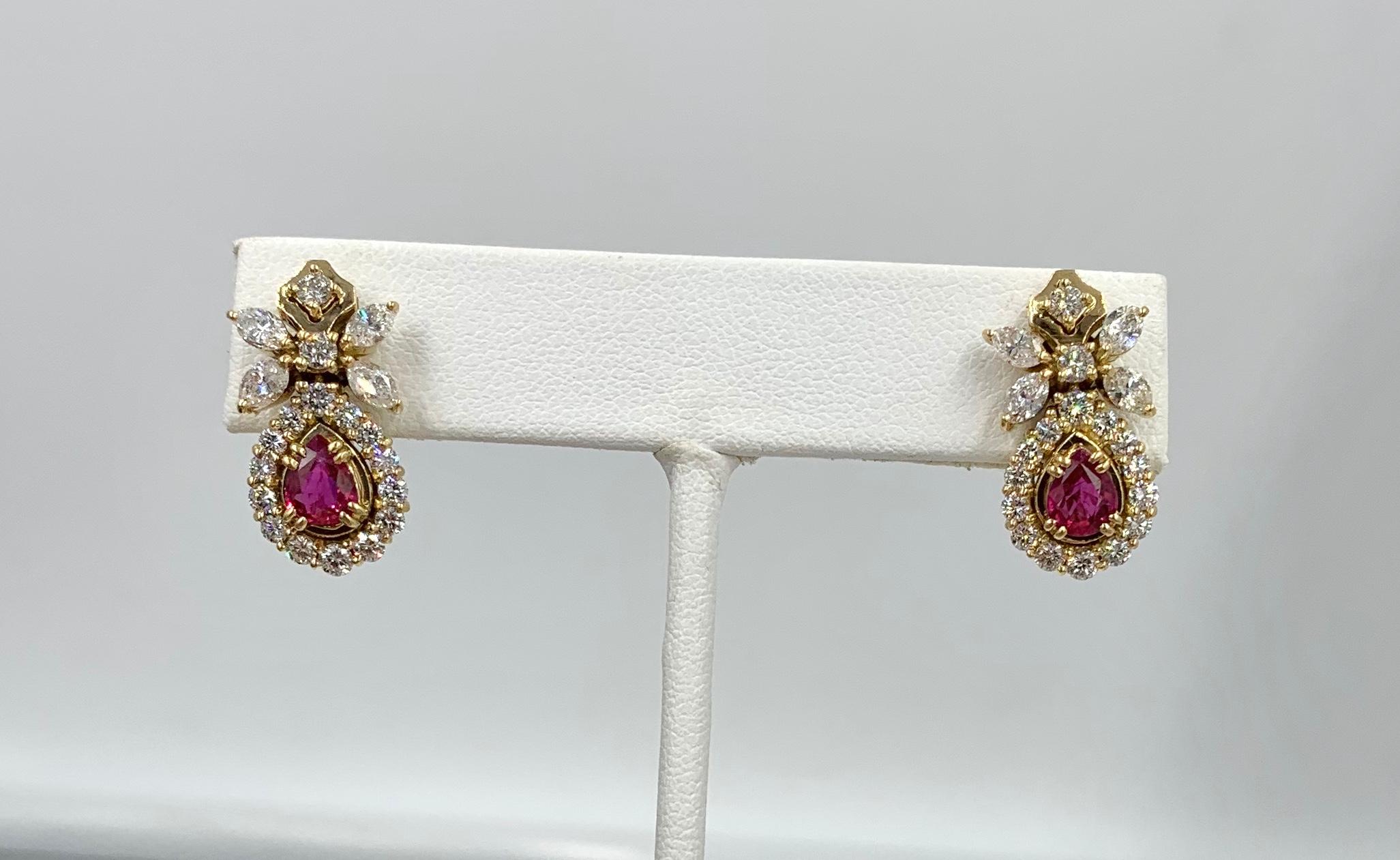 A magnificent pair of Pear Shape Ruby and Diamond Halo Flower Motif Drop Dangle Earrings in 18 Karat Gold.   The delightful jewels feature gorgeous Pear Shape Fine Red Rubies.  The Rubies total .87 Carats and have wonderful red color and fire.  The
