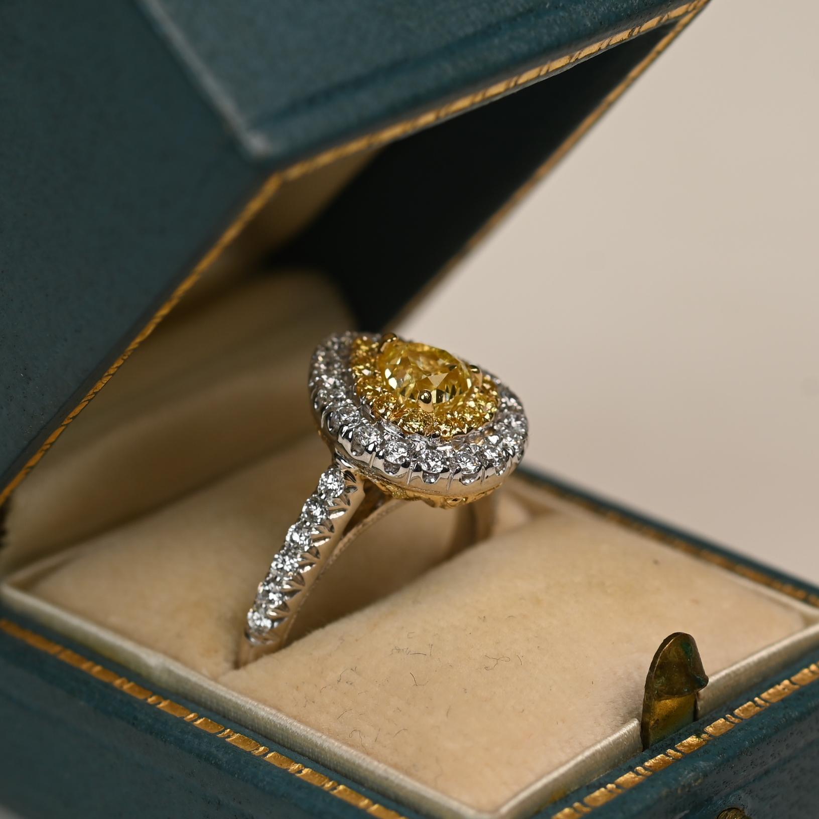 This ring centers an approximately 0.80 carat pear-shaped yellow diamond of VS2 clarity, secured in a yellow gold prong setting. The vibrant center stone is framed by a double halo of yellow and white diamonds, enhancing both its brilliance and