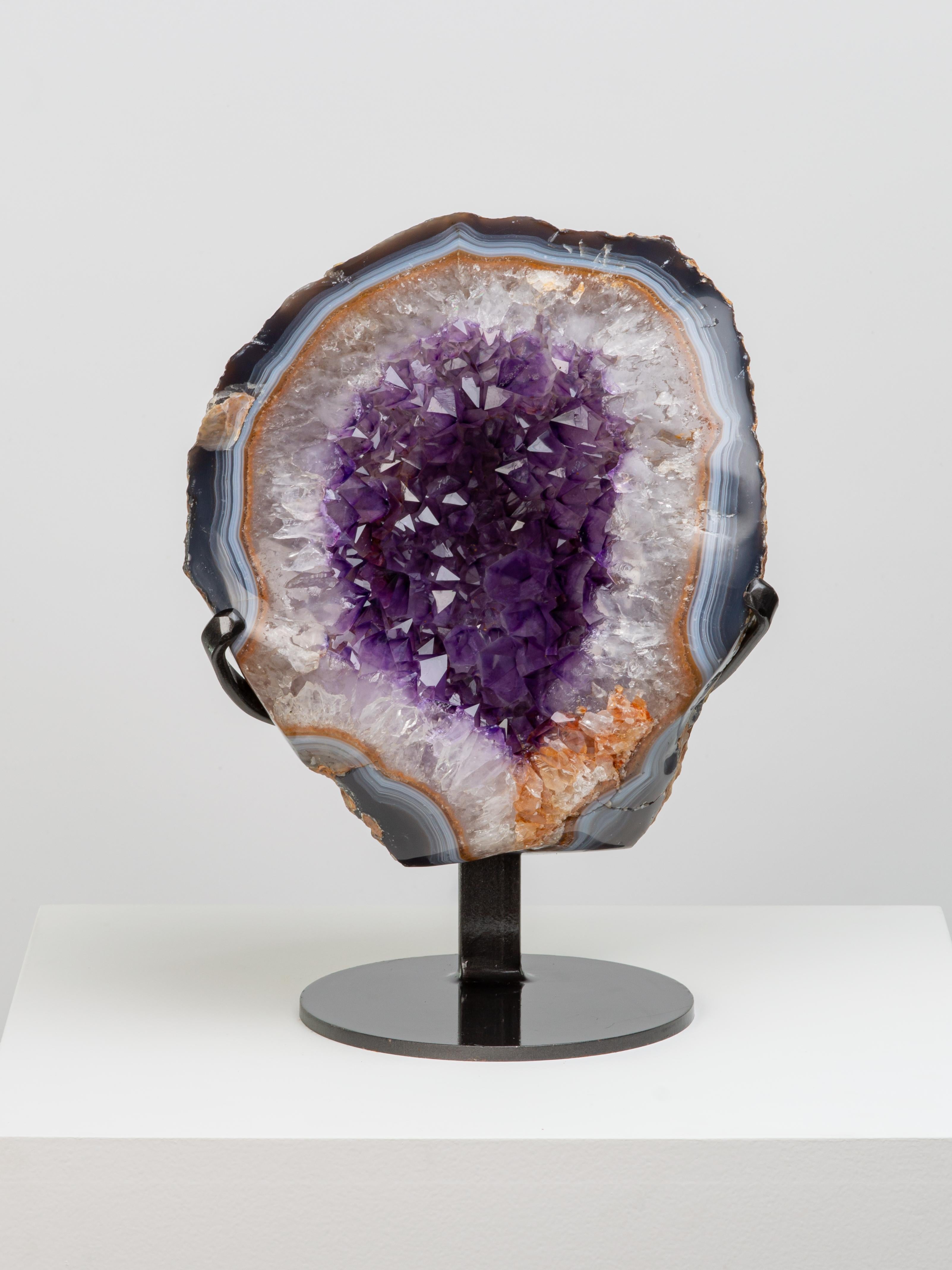 This beautiful half geode has a wonderful blue-brown banded agate border
with a thick base of white quartz differentiating to deep amethyst at the tips. 
A small section of orange quartz crystals can be admired at the bottom right.

This piece
