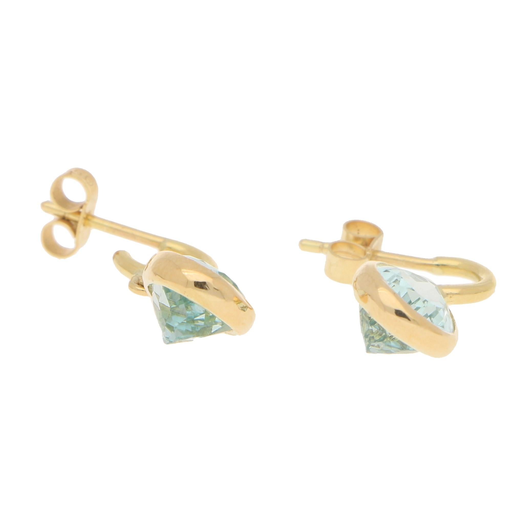 A lovely pair of pear-shaped aquamarine half hoop earrings set in 18k yellow gold. Each earring features a singular aquamarine encased in a 18k yellow gold rubover setting. The stones are then attached to a simple solid half hoop earring which have