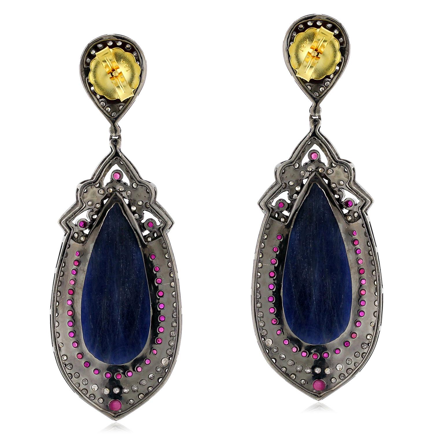 These beautiful pear-shaped blue sapphire earrings are a true masterpiece. The vibrant blue sapphires are the centerpiece of these earrings, and are surrounded by a halo of sparkling rubies. The earrings are finished with a 18k gold and silver