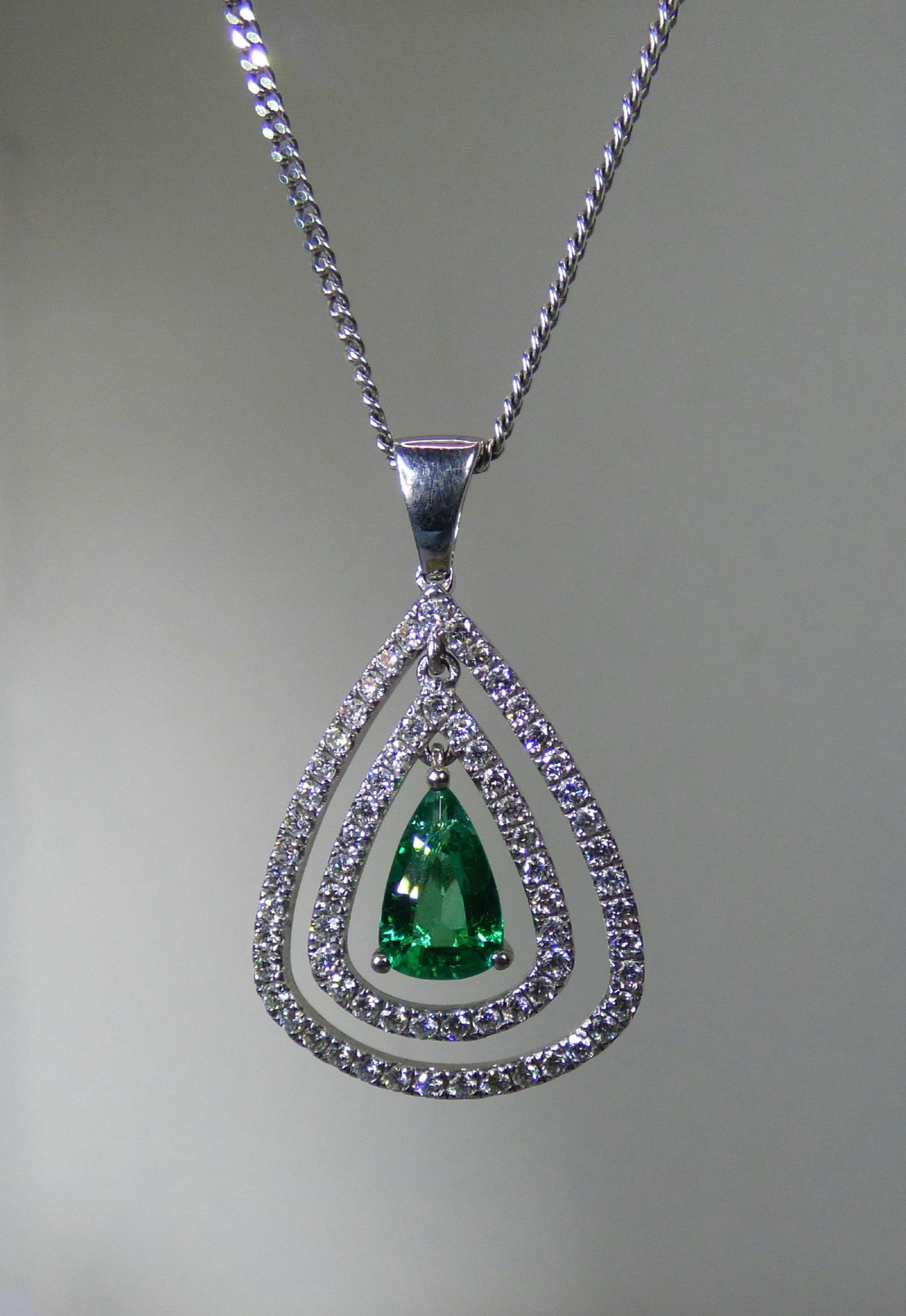 An untreated natural pear shaped Emerald (.88ct.) is surrounded by two Diamond (.69ct. total Diamond weight) set pear shapes. The total size is 20X18mm in a handmade 18K white gold pendant.  The pendant is hallmarked  by the Dublin Assay Office.