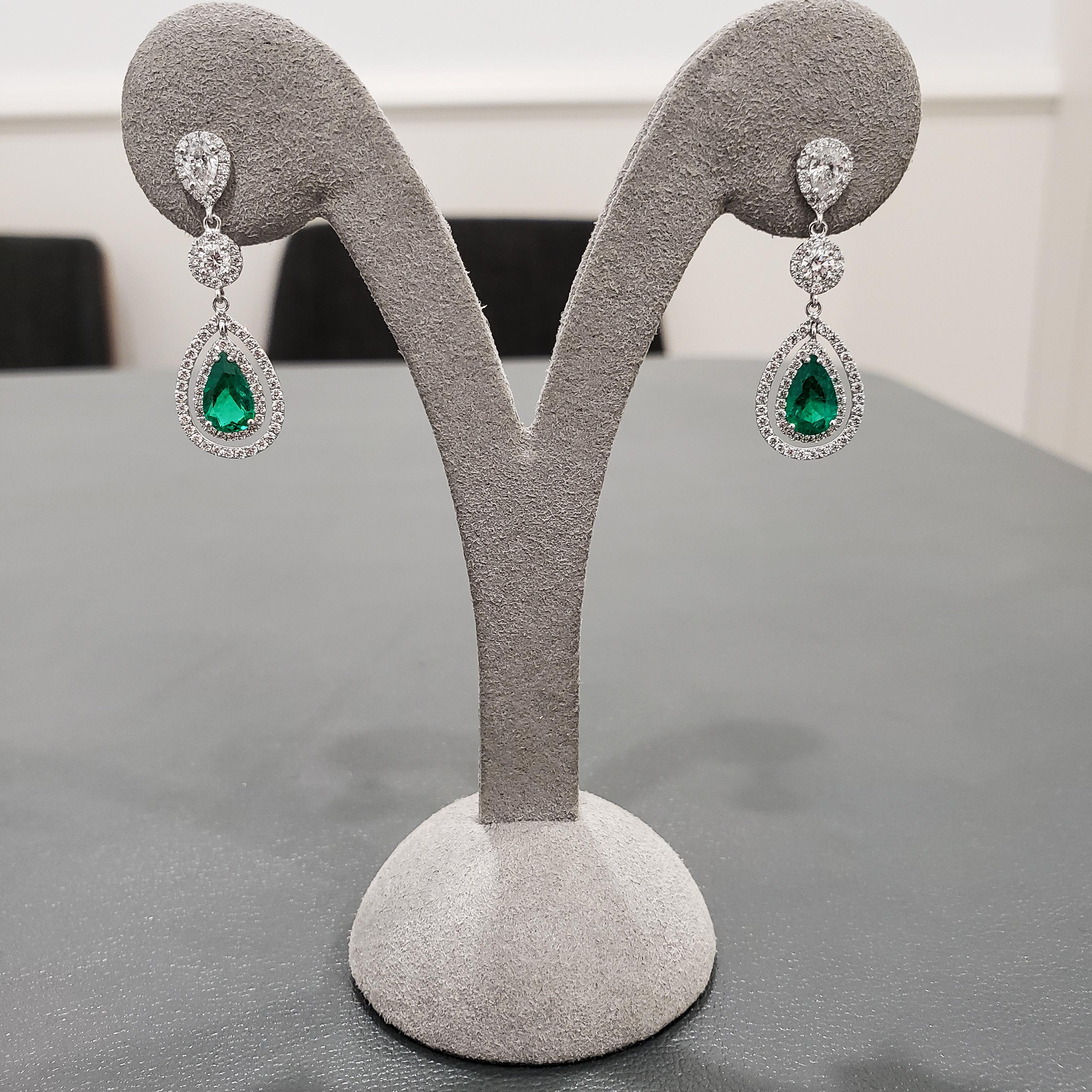 A gorgeous piece of 18k white gold dangle earrings featuring a color-rich pear shaped green emerald weighing 1.38 carats total. Each emerald elegantly set in an open work double halo diamond surround. Suspended on a pear shaped diamond halo and