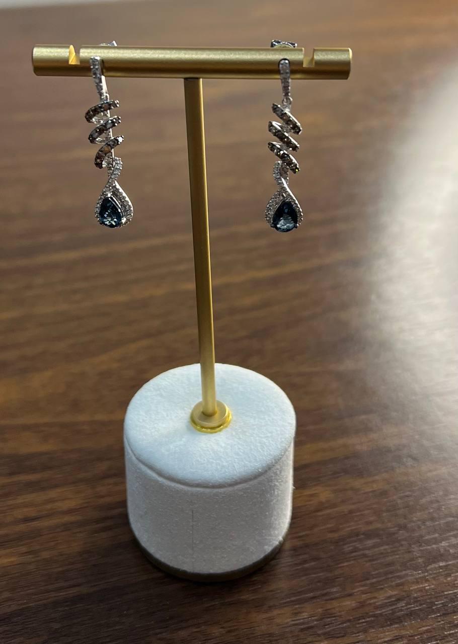 Elegantly crafted in white gold, these earrings feature a spiral design adorned with shimmering diamonds. Each earring culminates in a teardrop-shaped blue sapphire, encircled by a halo of sparkling diamonds. The intricate spiral motif adds a