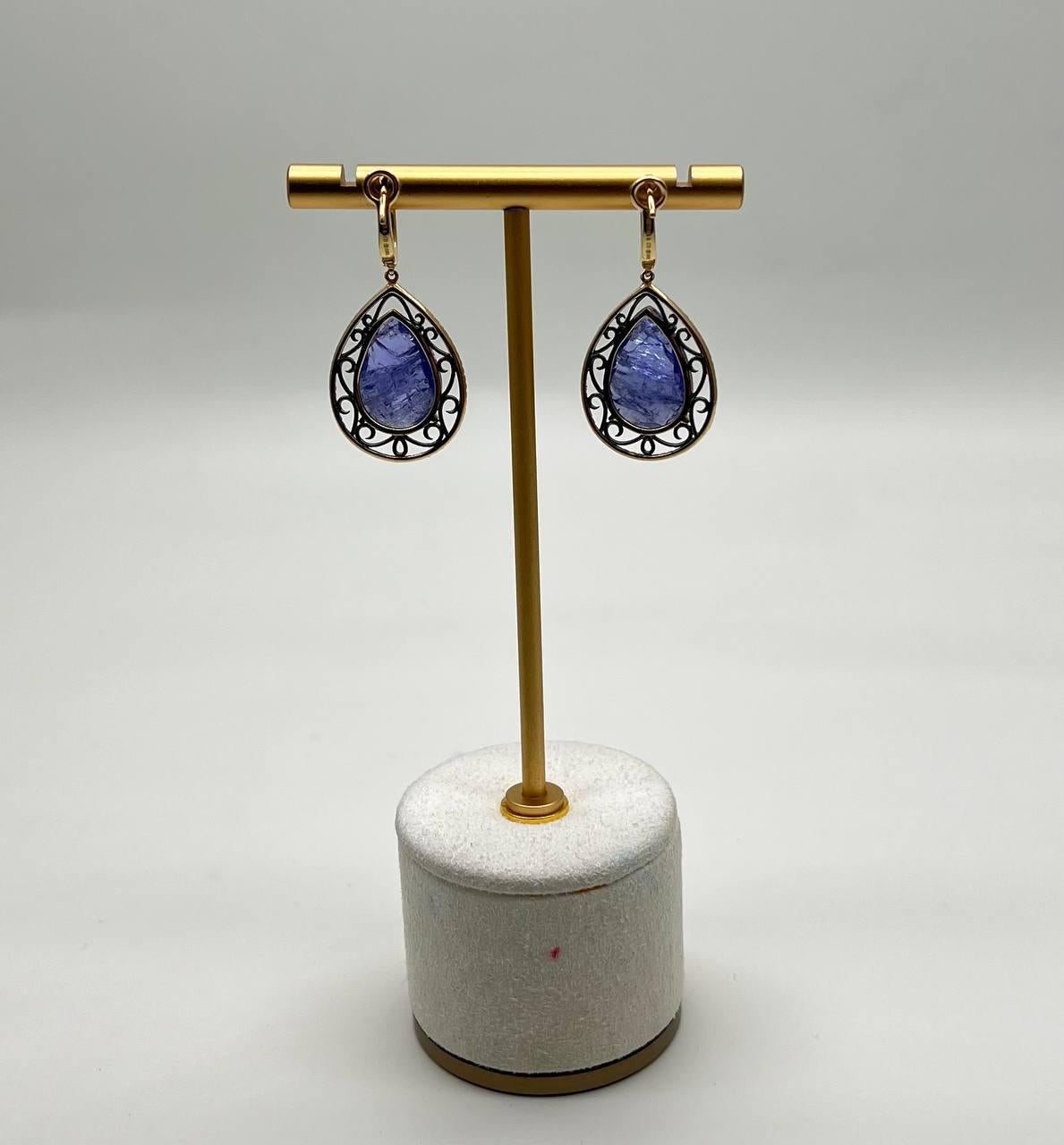 A striking and elegant pair of earrings. These earrings feature teardrop-shaped violet blue tanzanite stones, each set in an intricate 14k gold frame.

The metalwork includes delicate filigree details, adding a touch of sophistication, with diamond