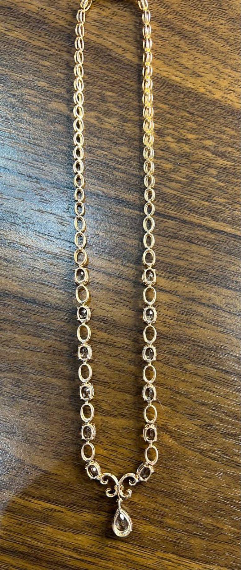 Questa squisita collana è realizzata in modo artigianale. Il design è caratterizzato da una serie di maglie ovali, ciascuna con diamanti scintillanti. Il centro è costituito da un motivo a volute ornato da un ciondolo con gemma a forma di goccia.
