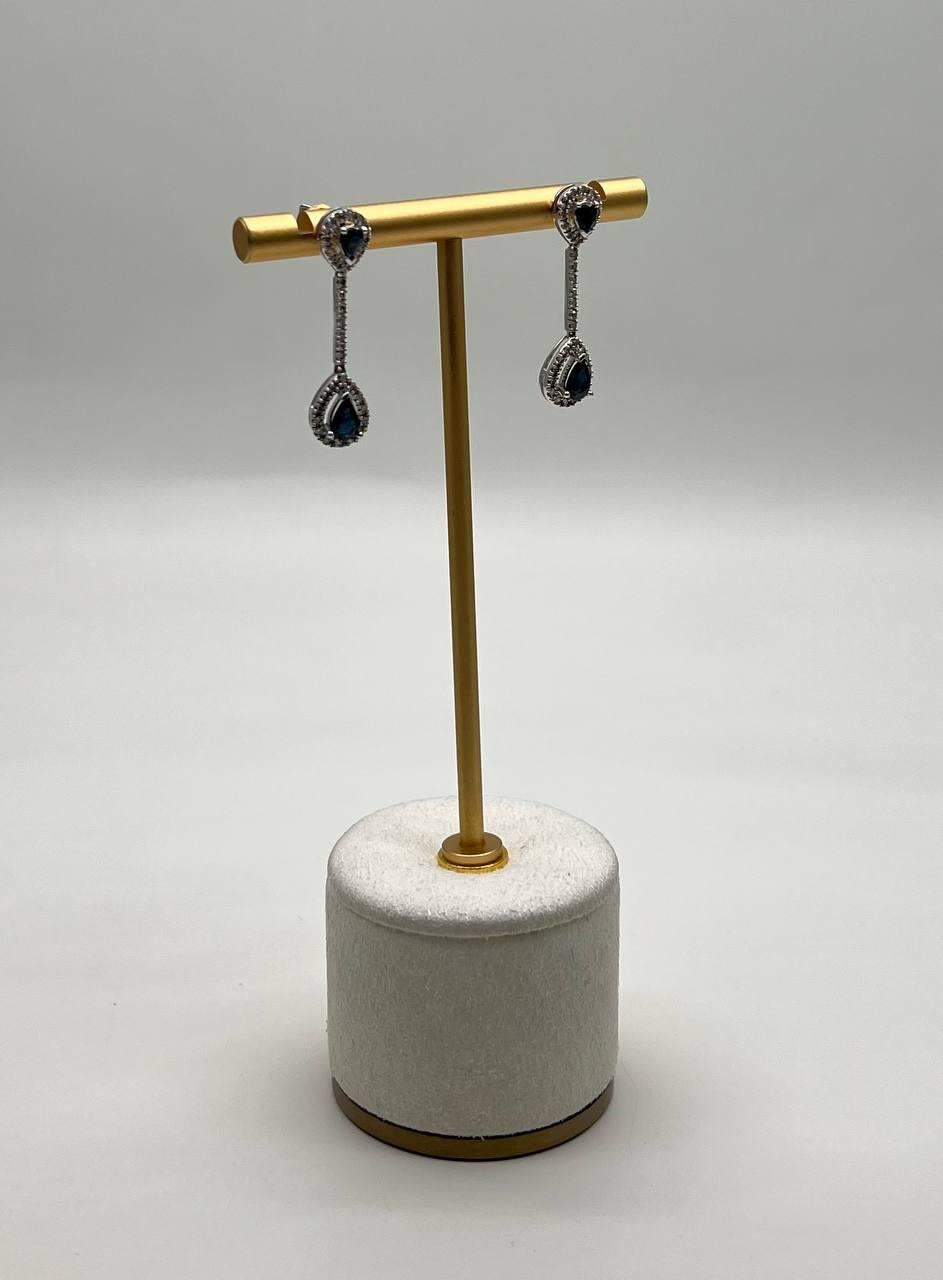 Elegant earrings . Each earring features a teardrop-shaped blue sapphire, surrounded by a halo of sparkling clear diamonds.
The stones are connected by a slender, shimmering line of clear diamonds, creating a graceful drop effect.
The design is both