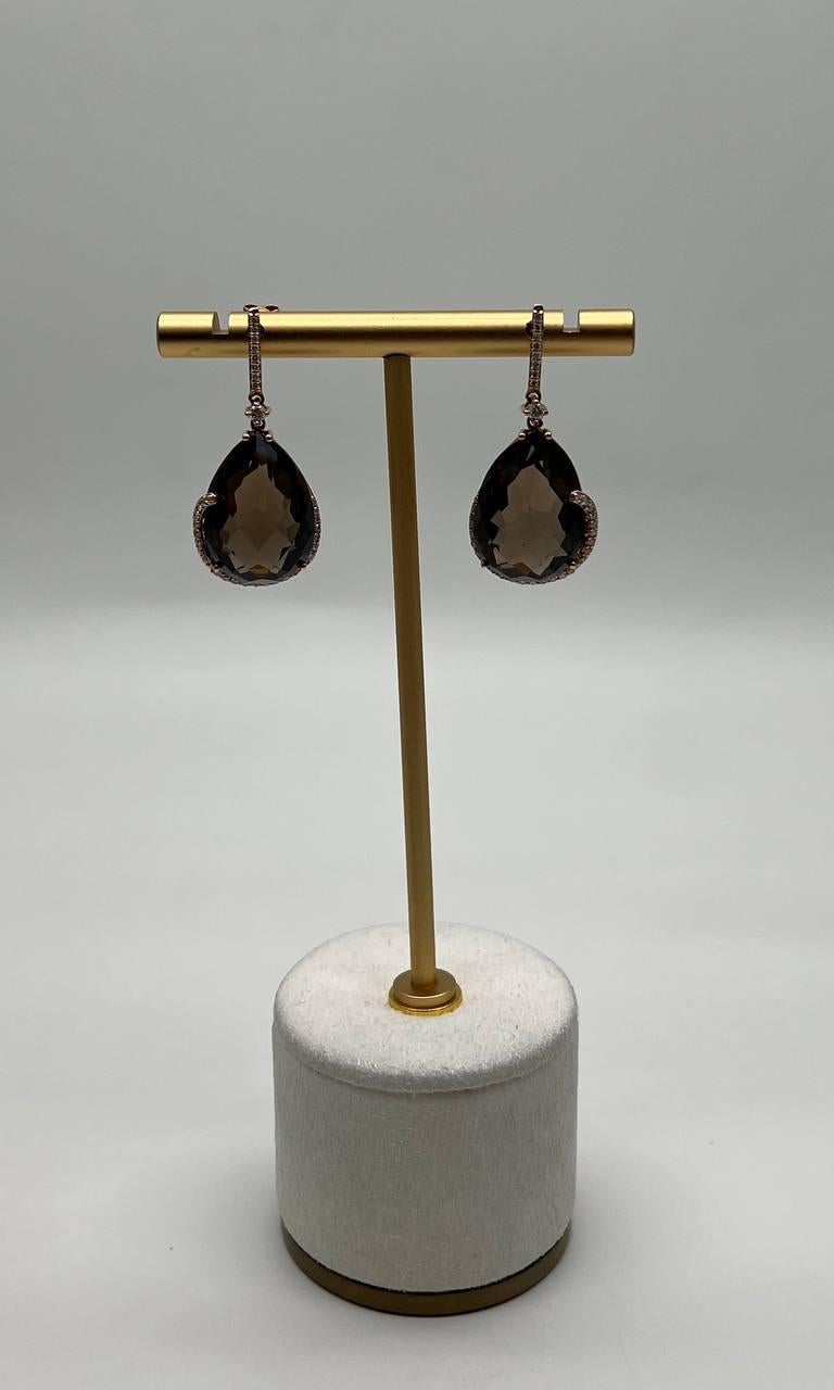 Questi eleganti orecchini a goccia sono caratterizzati da un grande quarzo marrone sfaccettato a forma di goccia, elegantemente sospeso a delicati ganci. Le pietre sono circondate da un sottile bordo scintillante che aggiunge un tocco di
