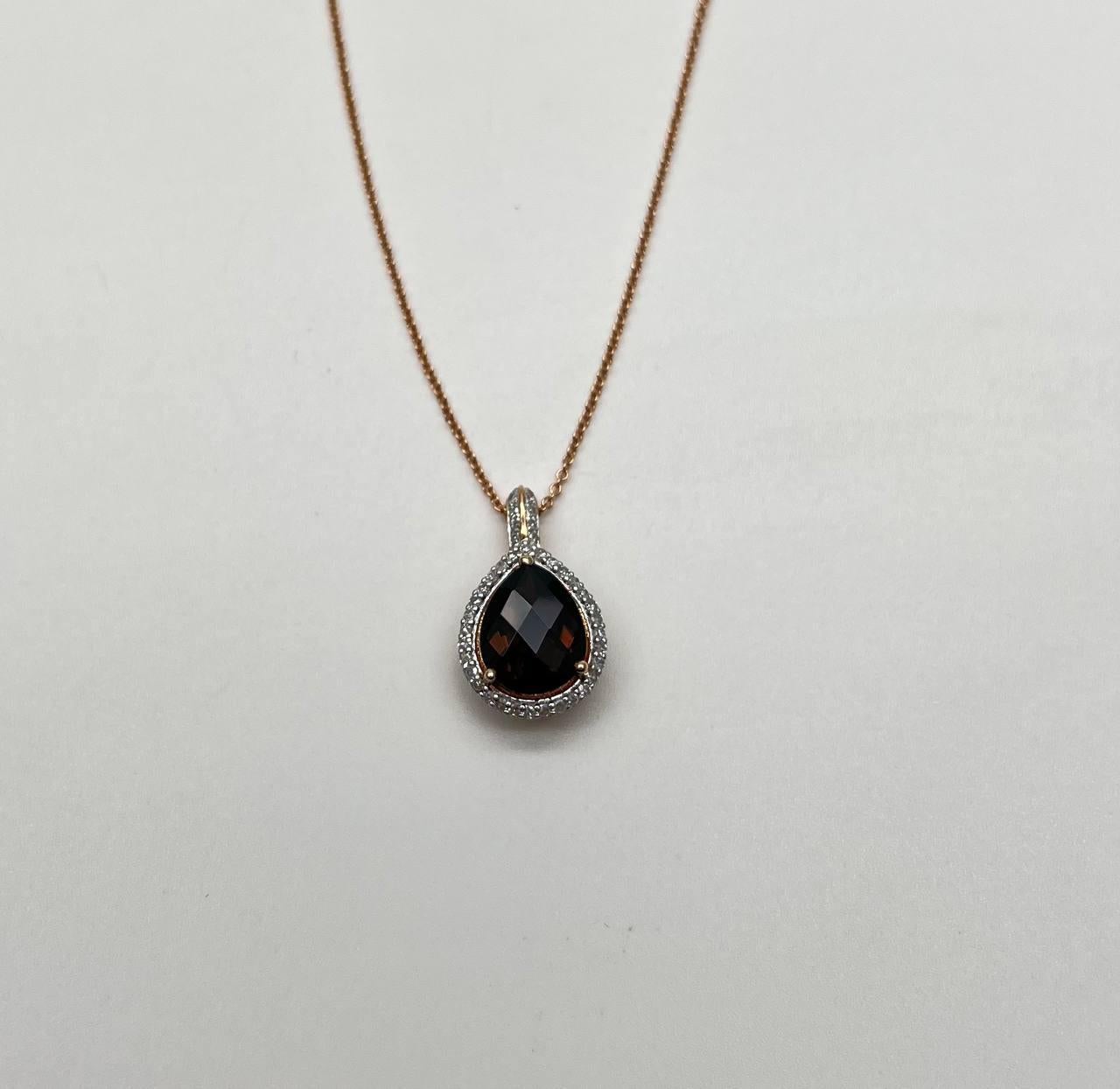 Prova il fascino raffinato di questa collana con ciondolo. La collana presenta un ciondolo a goccia in quarzo marrone fumé con una gemma scura sfaccettata, circondata da un'aureola di diamanti scintillanti. Il ciondolo è sospeso a una delicata