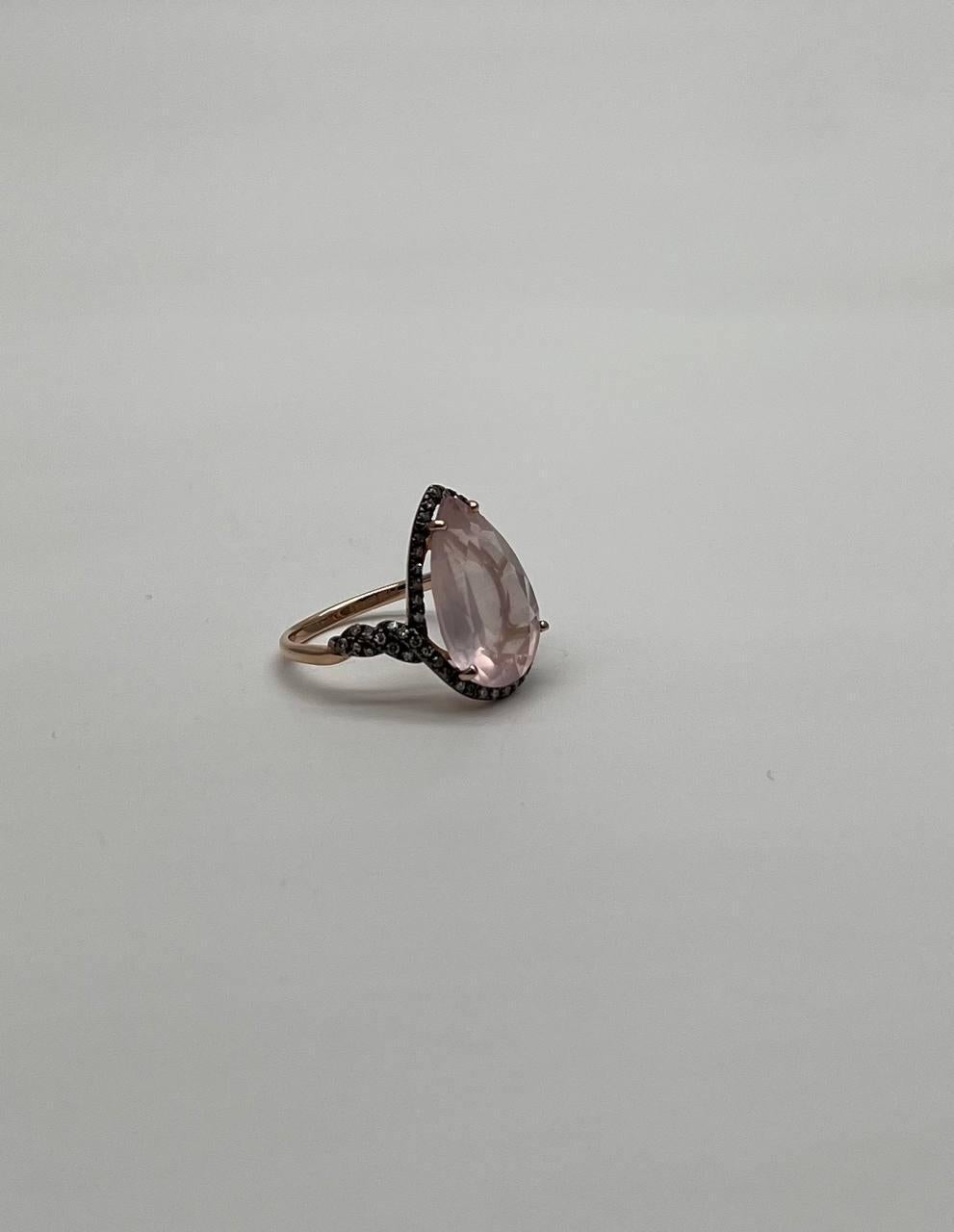 Questo squisito anello presenta un grande quarzo rosa a forma di pera incastonato in una delicata fascia. La gemma è circondata da un'aureola di piccoli diamanti color champagne scuro, che aggiungono contrasto e profondità. La fascia è intricata con