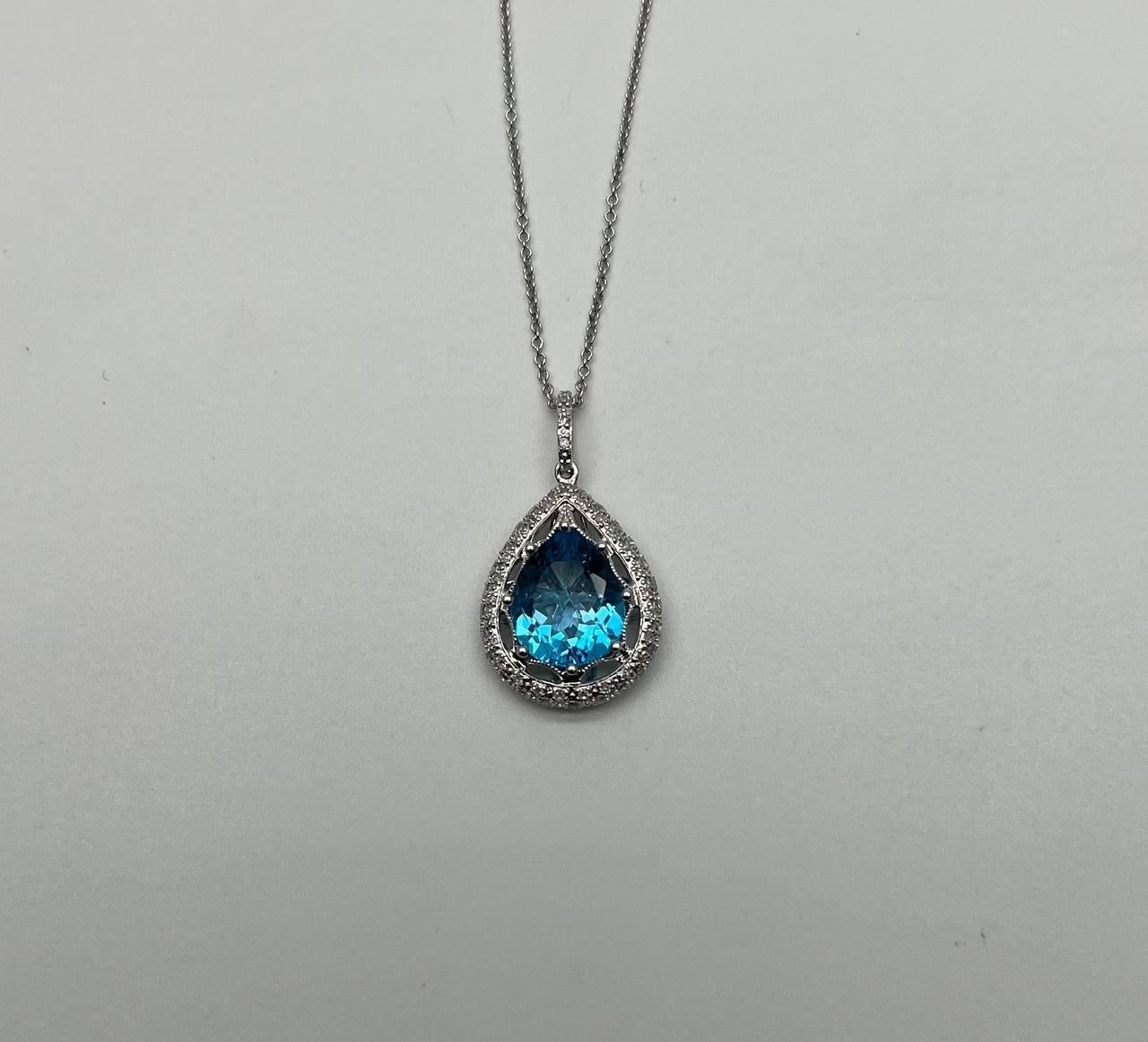A stunning Swiss Blue Topaz pendant necklace.
It features a pear-shaped blue gemstone with a vibrant oceanic hue. Surrounding the gemstone is a halo of sparkling round-cut diamonds, enhancing its brilliance.
The pendant is suspended from a delicate