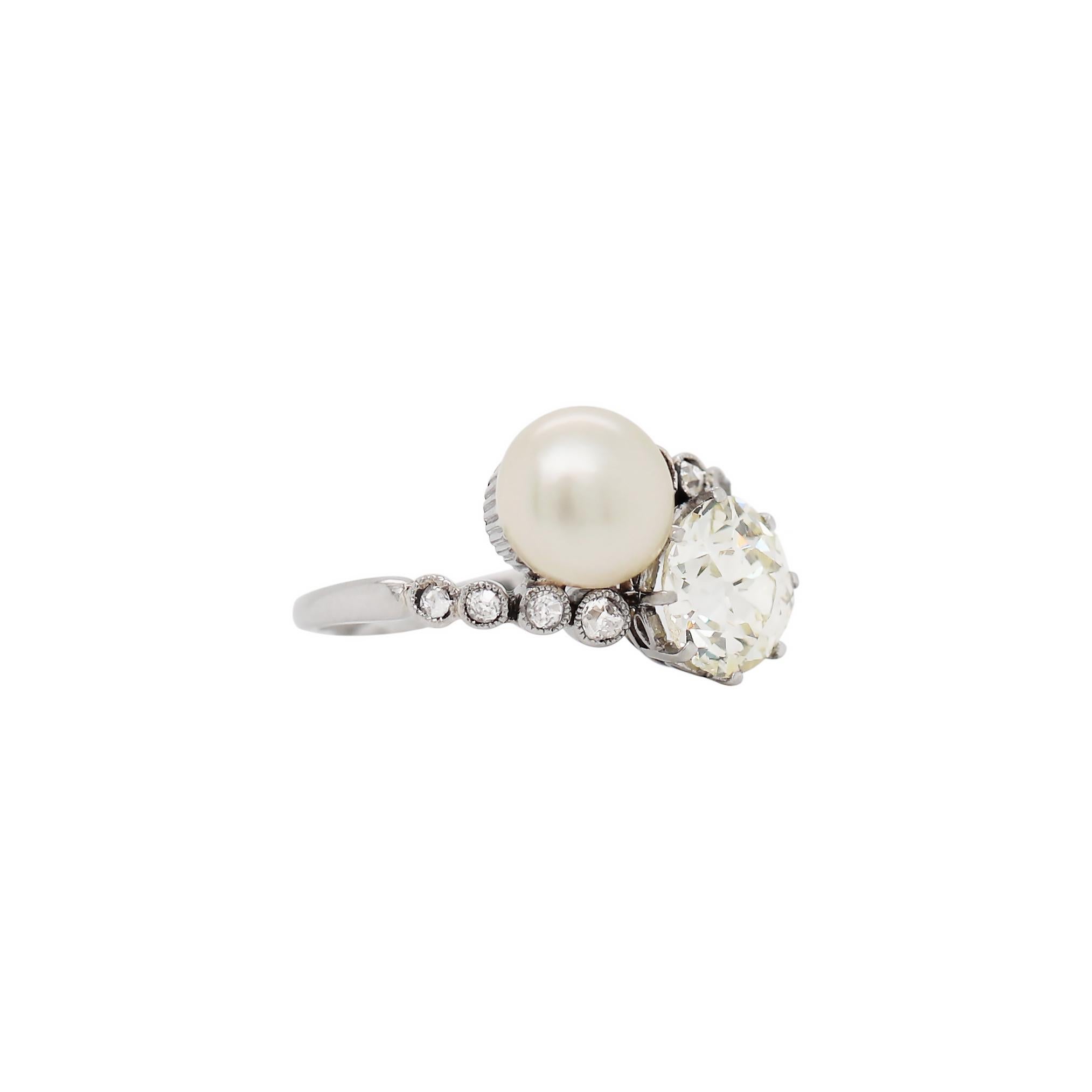 This incredible antique crossover engagement ring features an old cut diamond weighing 1.69ct, set in an eight claw open back setting. The diamond is beautifully accompanied by a natural saltwater button-shaped pearl measuring 7.5mm. The ring is