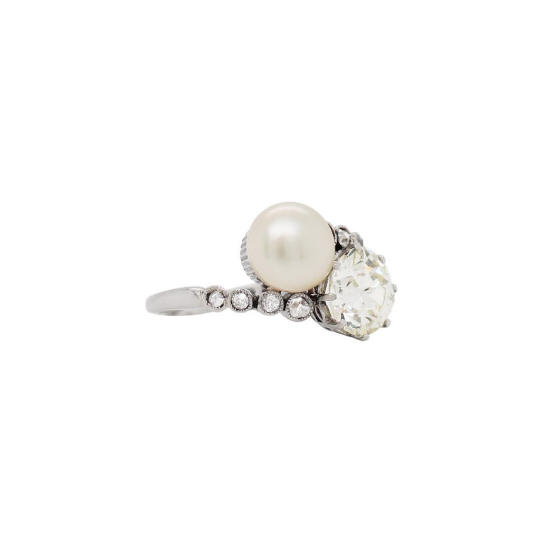This incredible antique crossover engagement ring features an old cut diamond weighing 1.69ct, set in an eight claw open back setting. The diamond is beautifully accompanied by a natural saltwater button-shaped pearl measuring 7.5mm. The ring is