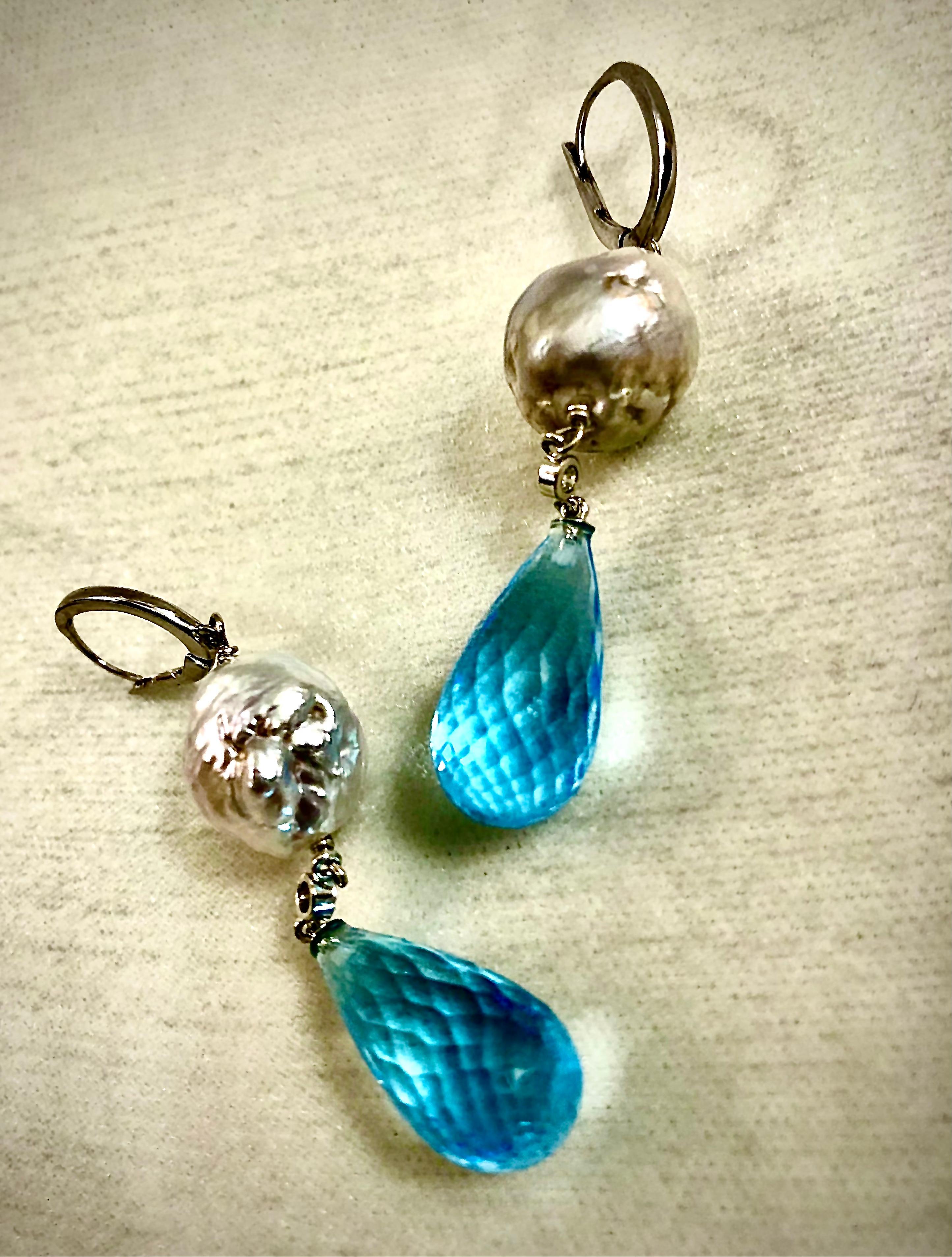 Elegant long earrings in 14kt white gold. A large semi round pale grey baroque freshwater pearl anchors the top of this jewel. Suspended from the pearls is a small bezel set from hangs a large, faceted teardrop shaped sky-blue topaz. The are