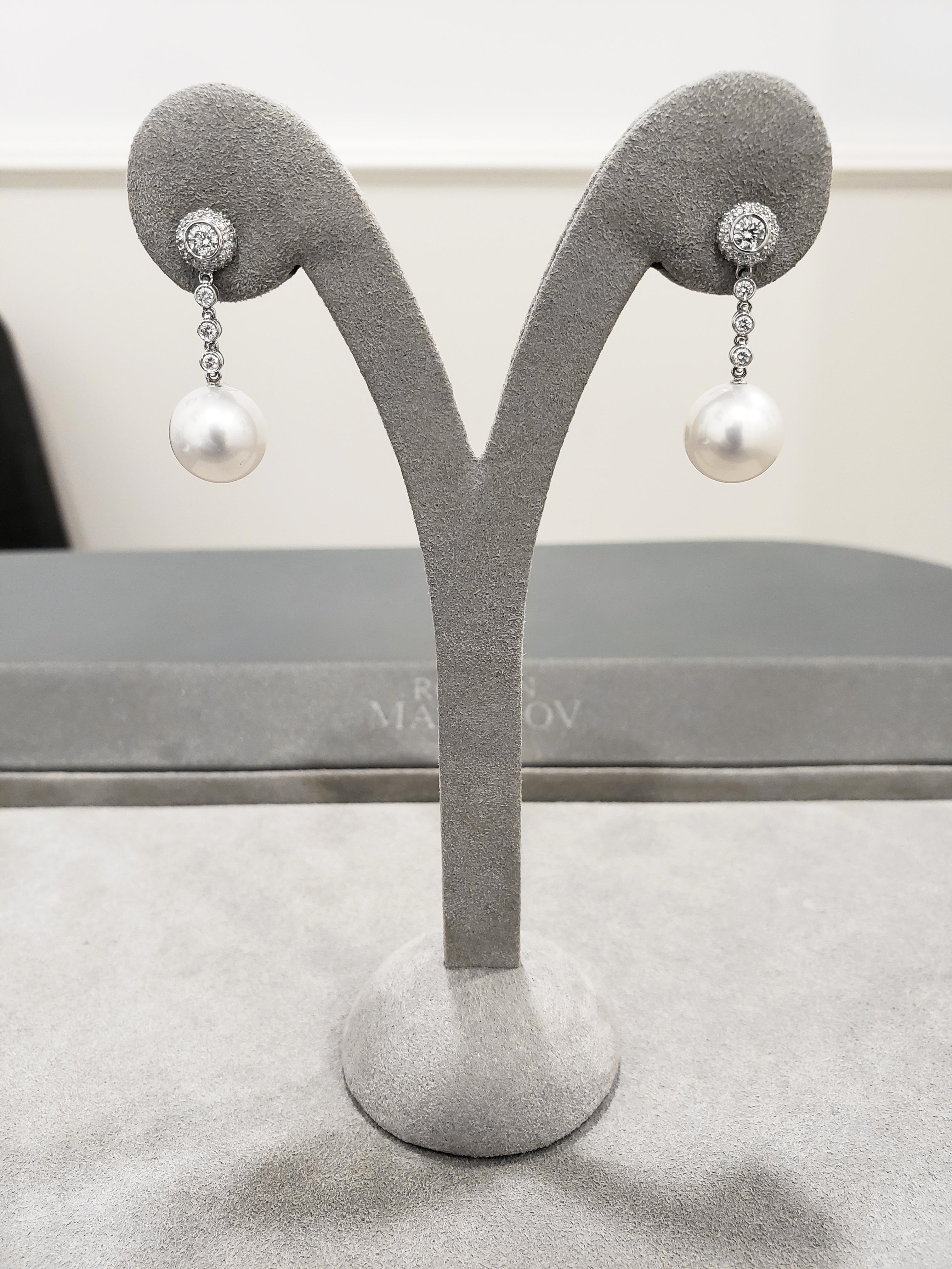 A classy pair of drop earrings showcasing two white fresh water pearls gracefully suspended on a diamonds by the yard design in bezel set diamonds. Attached to a pave set and cluster diamond earring post. Diamonds weigh 0.69 carats total. Made in