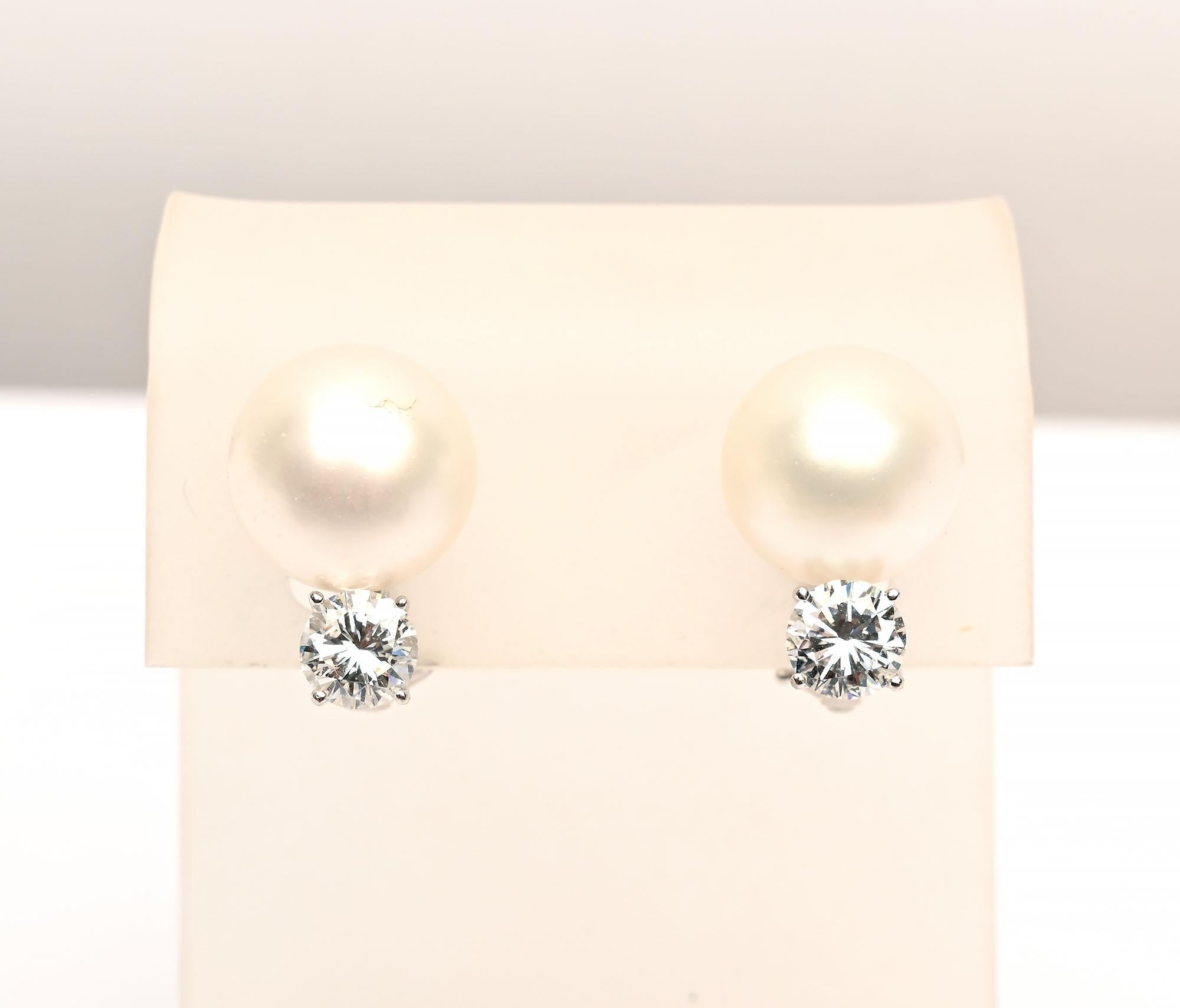 Elegant pearl earrings, each with a 1 carat round brilliant diamond. One diamond is GIA rated as F color and VS2 quality. The other is E color and SI 1 quality. The GIA certification accompanies the earrings. Each pearl is slightly under 7 mm. 
The
