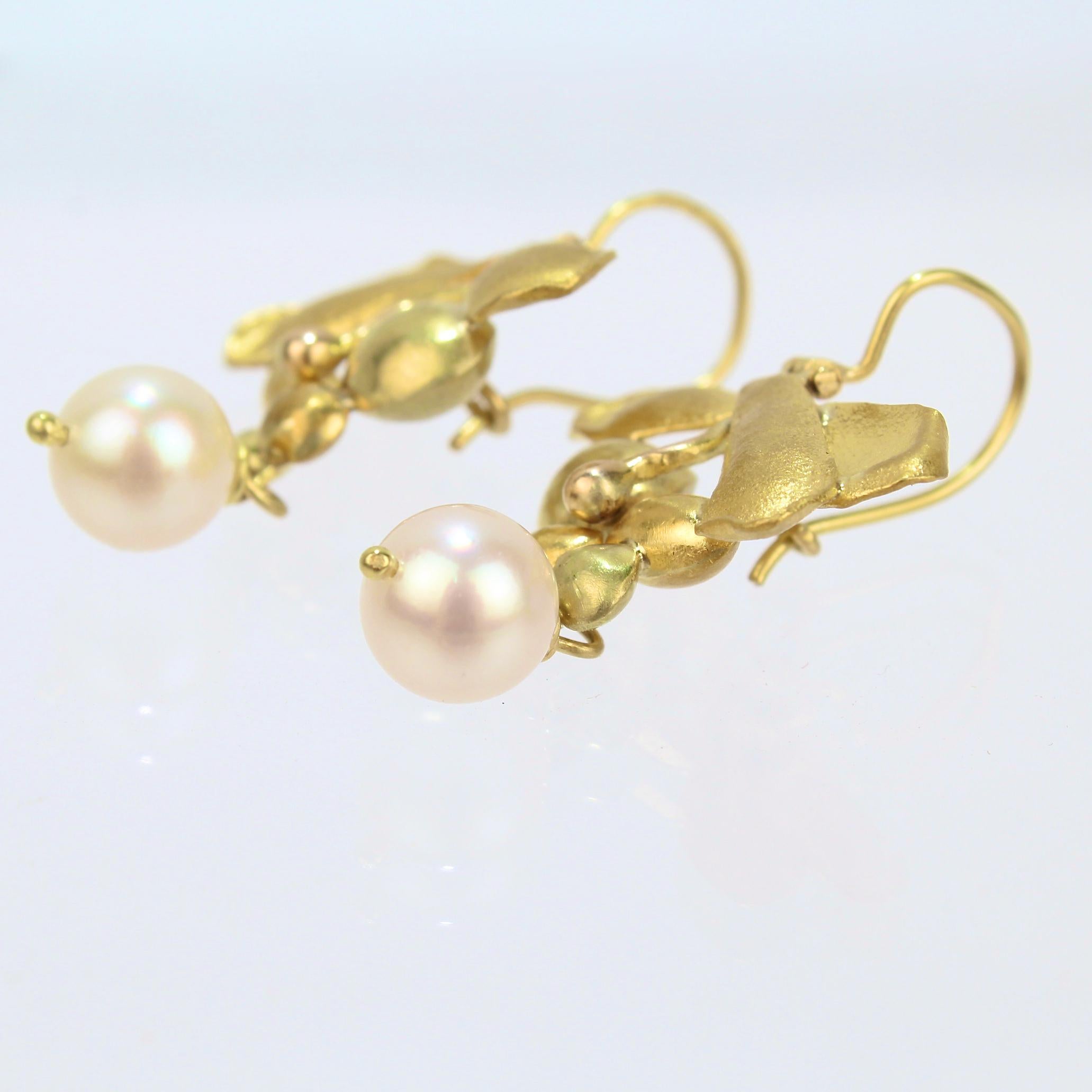 A very fine pair of modernist earrings in 22k gold.

Each earring has three textured leaf shapes that are set above round yellow and green seed or fruit shaped gold beads.  

A round white pearl is suspended from the bottom of each earring.

Simply