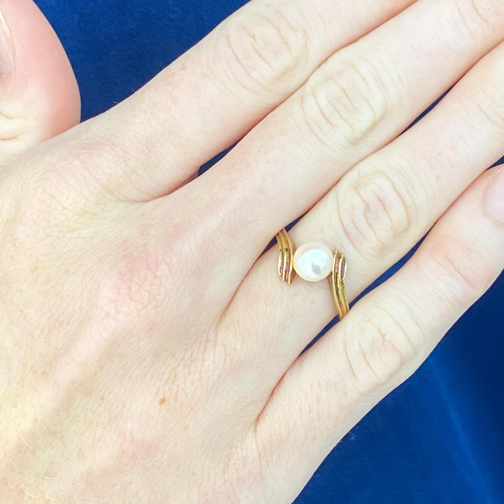 Dieser Bypass-Solitär-Perlenring besticht durch seinen fabelhaften Vintage-Stil. Die goldene Fassung umspielt die Perle anmutig wie Wellen auf dem Ozean, stützt sie und präsentiert sie, als würde sie zwischen ihnen schweben. Feiern oder ehren Sie