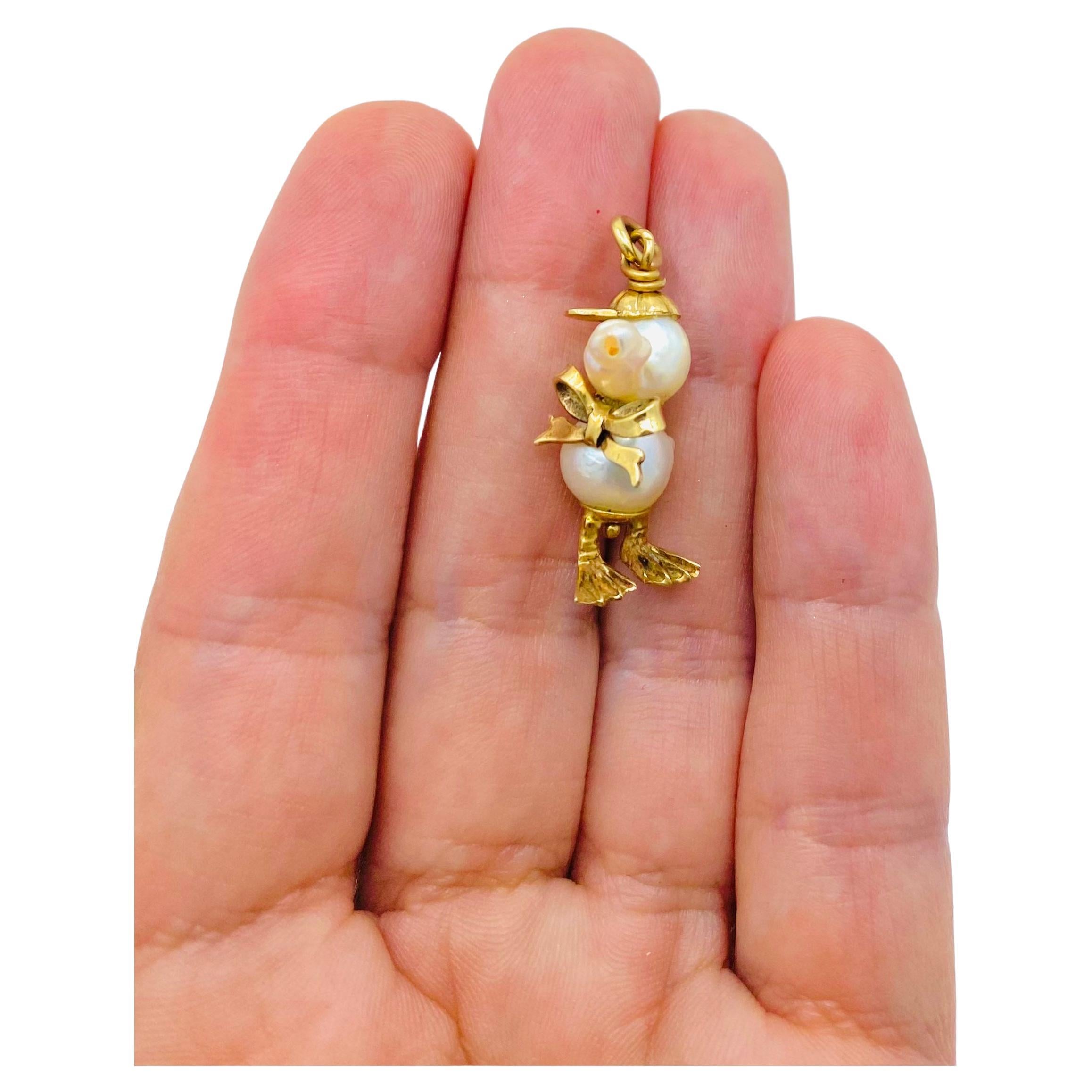Un adorable charm de patito de perlas, con oro de 10 quilates.
La cabeza y el cuerpo del patito están creados a partir de dos perlas unidas por el lazo dorado sentado
en el cuello del amuleto. La cabeza está rematada con una gorra de béisbol dorada,